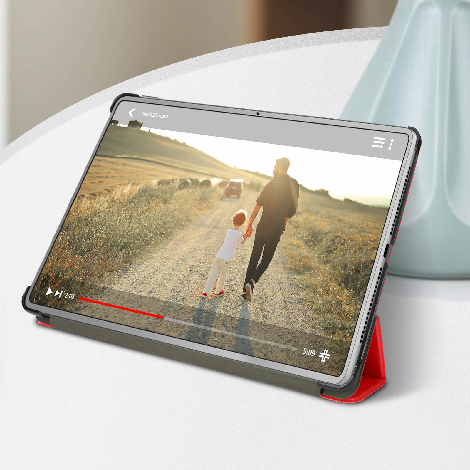 Tablet appoggiato in una custodia. Video in riproduzione sullo schermo. Tavolo e pianta visibili.