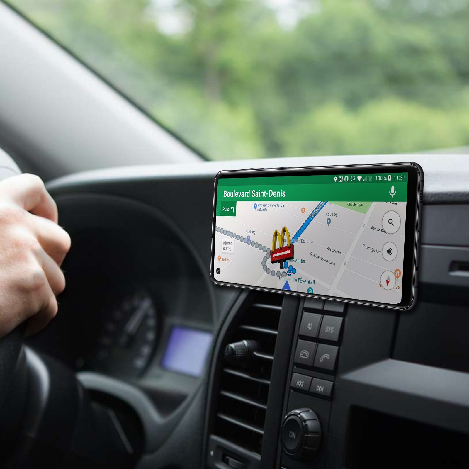 Telefon in Autohalterung mit Karte, Hand am Lenkrad. Fahrzeuginnenraum sichtbar.