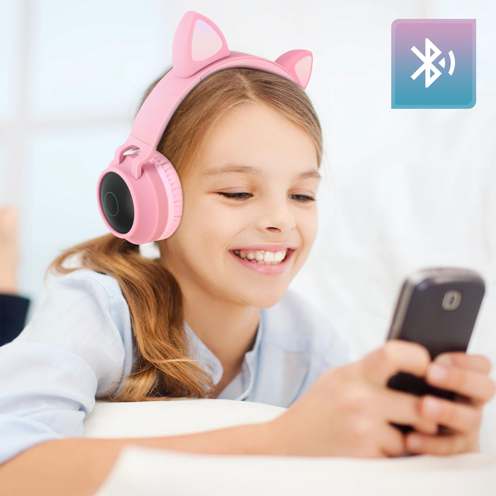 Ein junges Mädchen mit pinken Katzenohrkopfhörern lächelt auf ihr Handy.