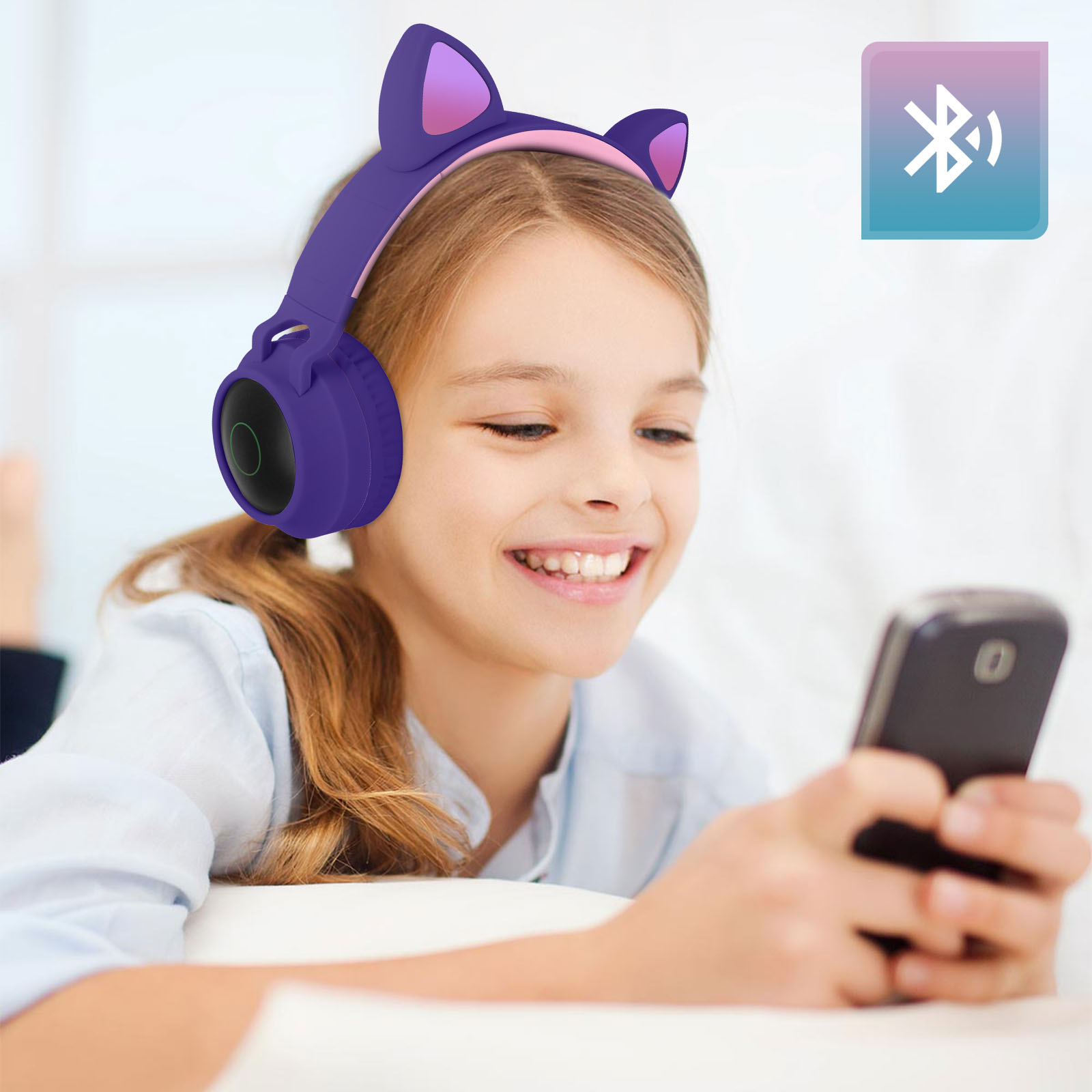 Ein Mädchen trägt lila Katzenohr-Kopfhörer und lächelt auf ein Telefon. Ein Bluetooth-Symbol ist sichtbar.