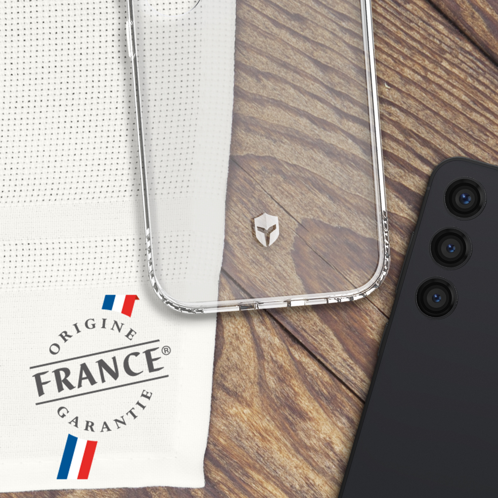 Una custodia per telefono, un telefono e un panno bianco con 'ORIGINE FRANCE GARANTIE' su legno.