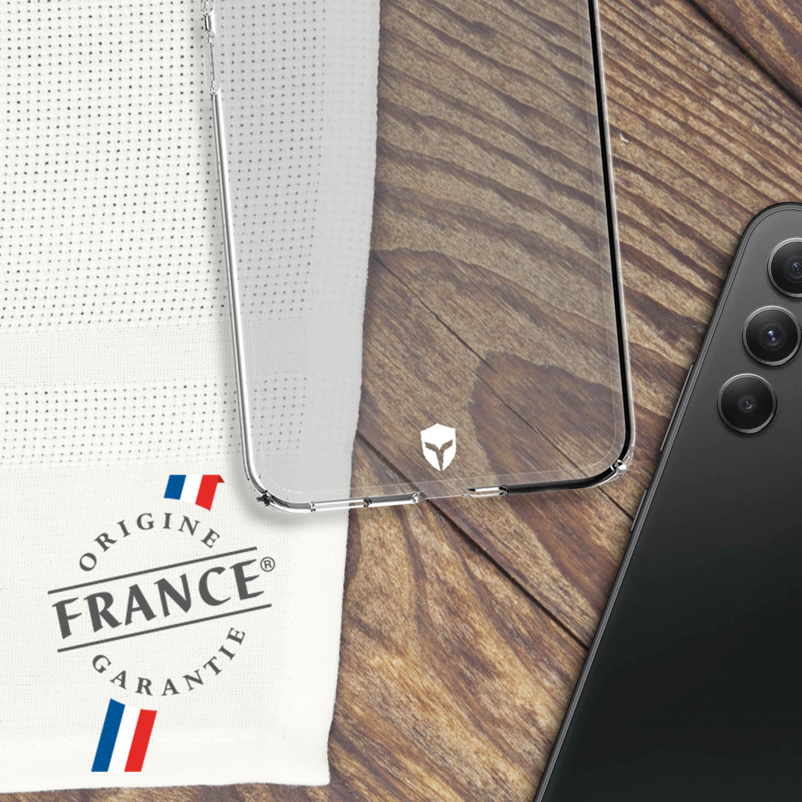 Klare Handyhülle über einem schwarzen Telefon. Ein weißes Handtuch mit 'Origine France'.