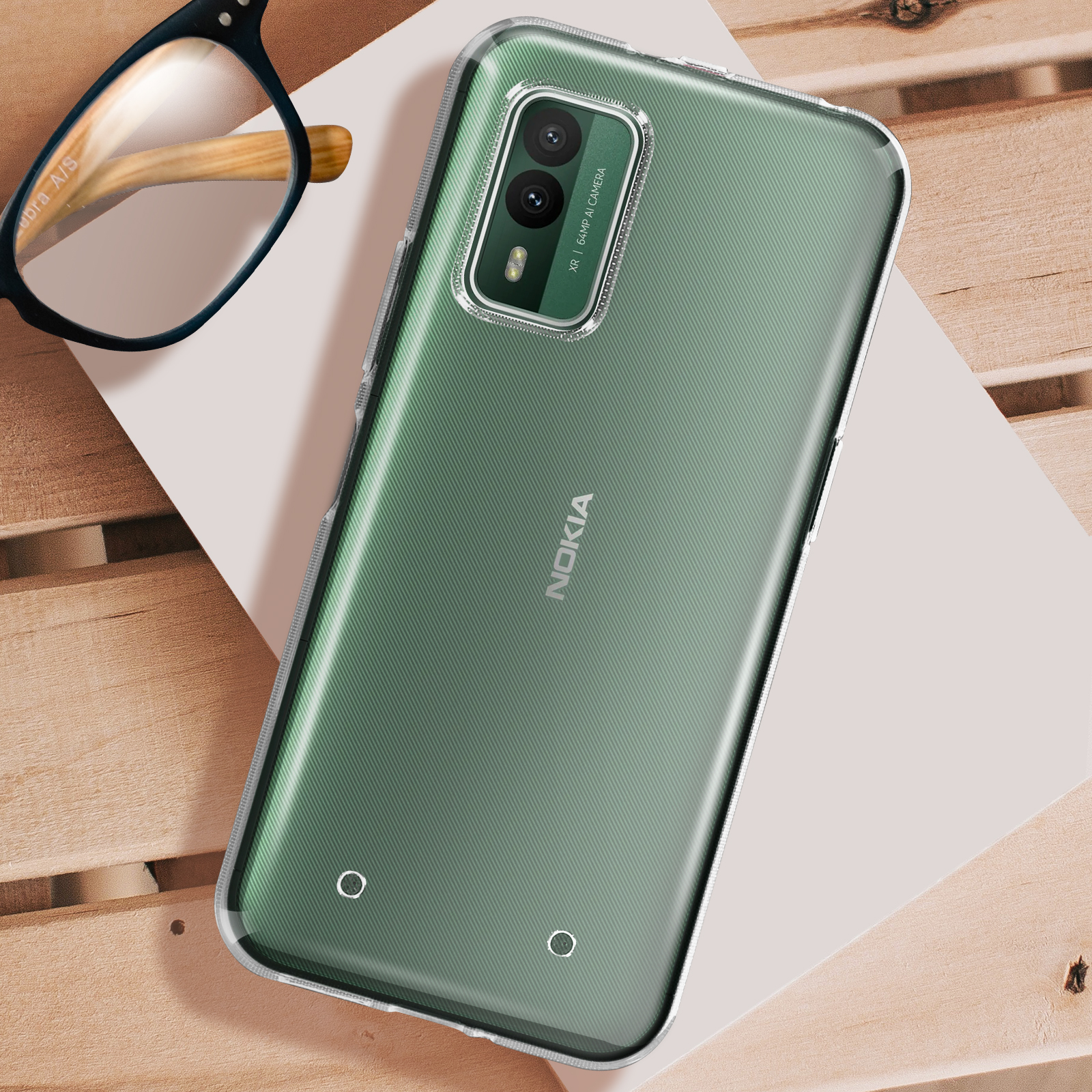 Telefono verde con custodia trasparente. Occhiali su superficie bianca. Sfondo con trama legno.
