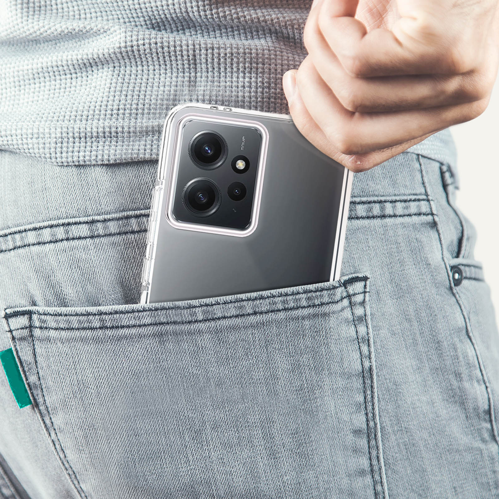 Un telefono in una custodia trasparente è in una tasca di jeans. Una mano raggiunge la tasca.