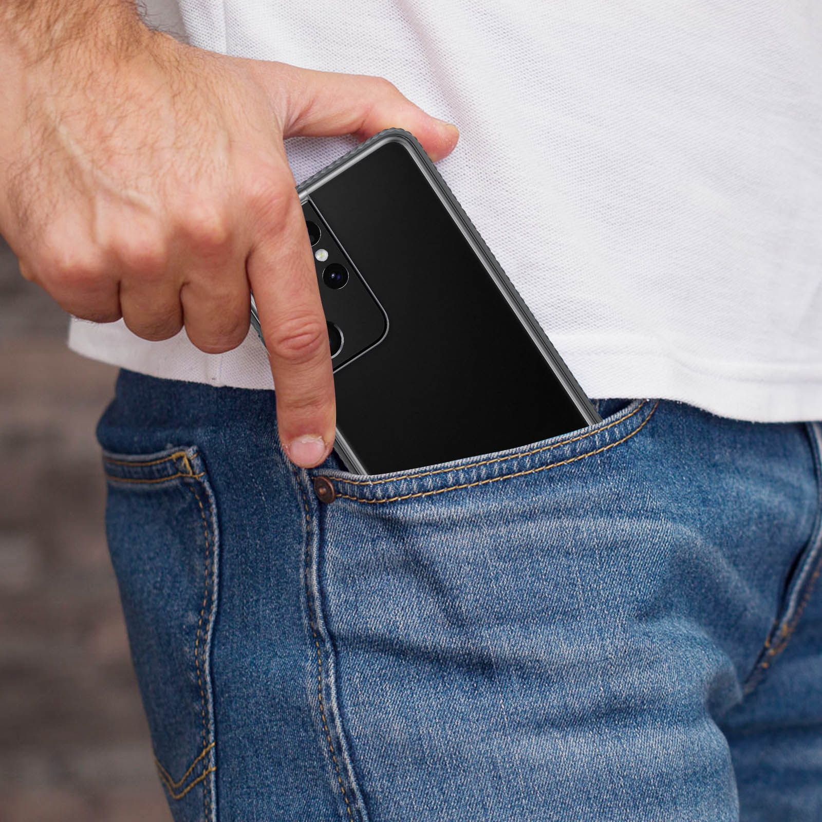 Eine Hand, die ein schwarzes Telefon in eine blaue Jeans-Tasche steckt. Die Rückseite des Telefons ist sichtbar.