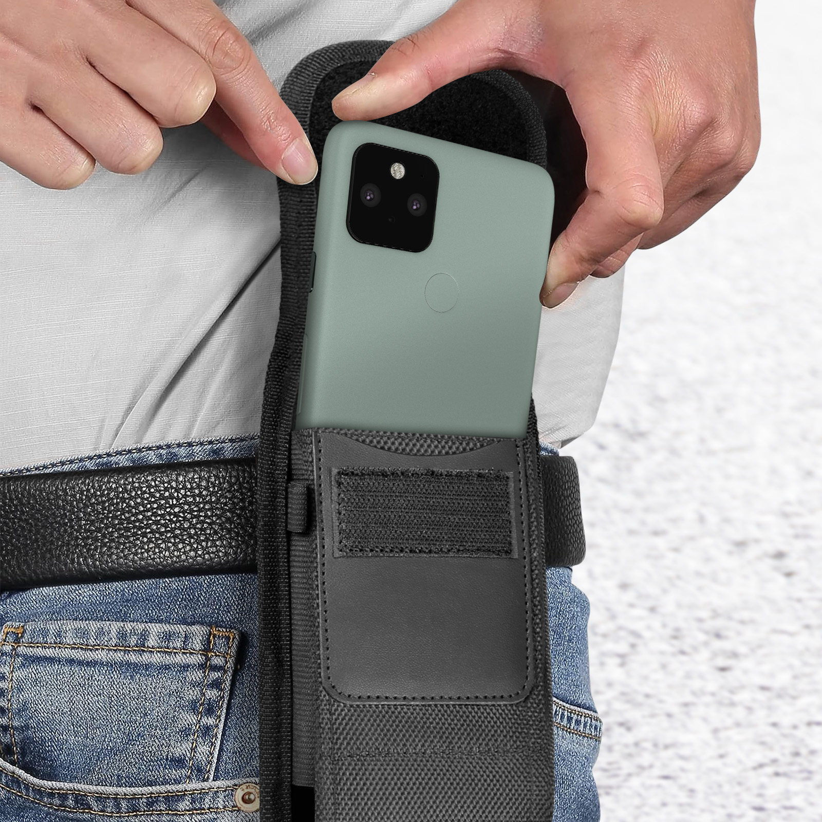 Persona che mette un telefono verde in una custodia da cintura nera. Sono visibili jeans e una cintura.