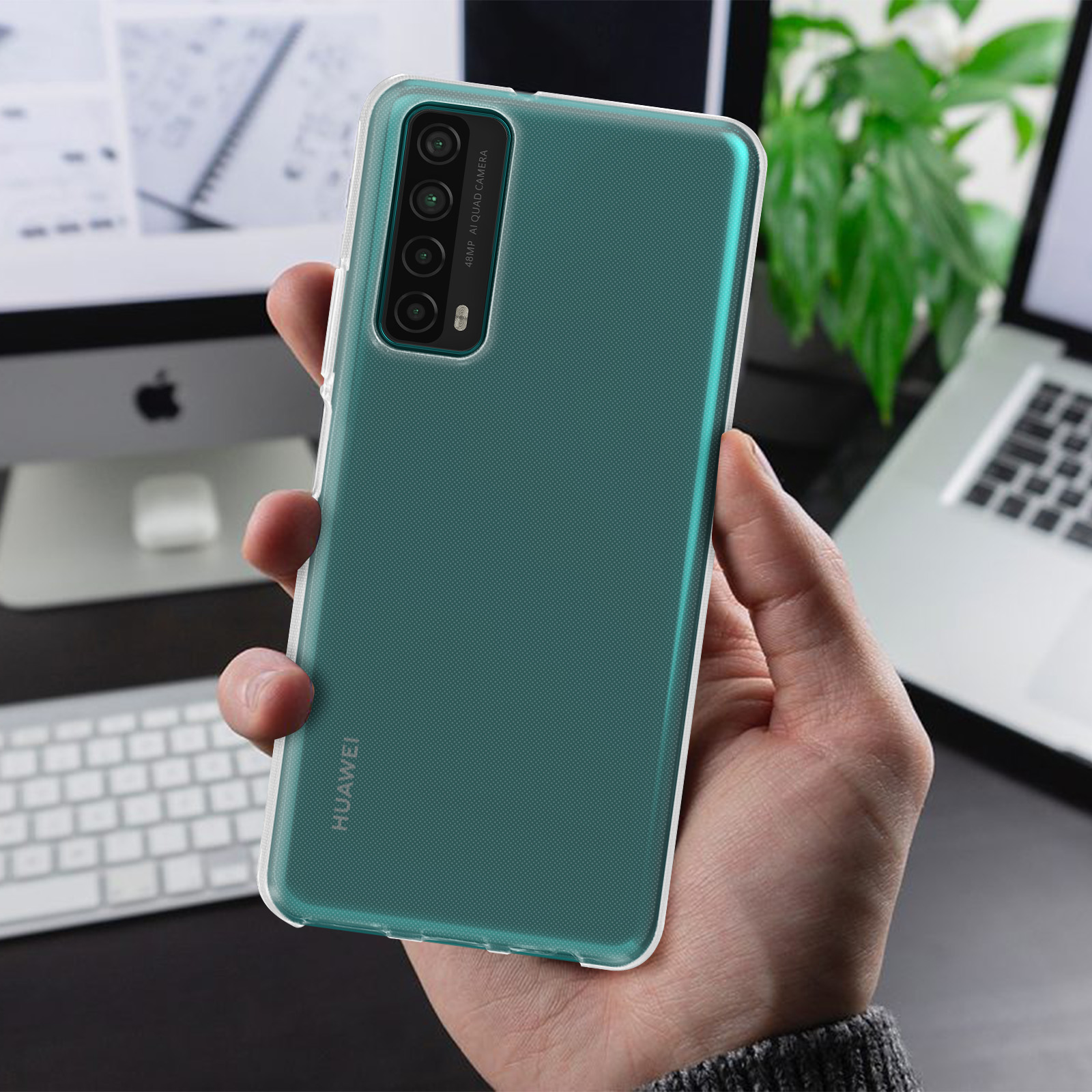 Dłoń trzymająca turkusowy telefon z przezroczystym etui na tle rozmytego tła z laptopem.