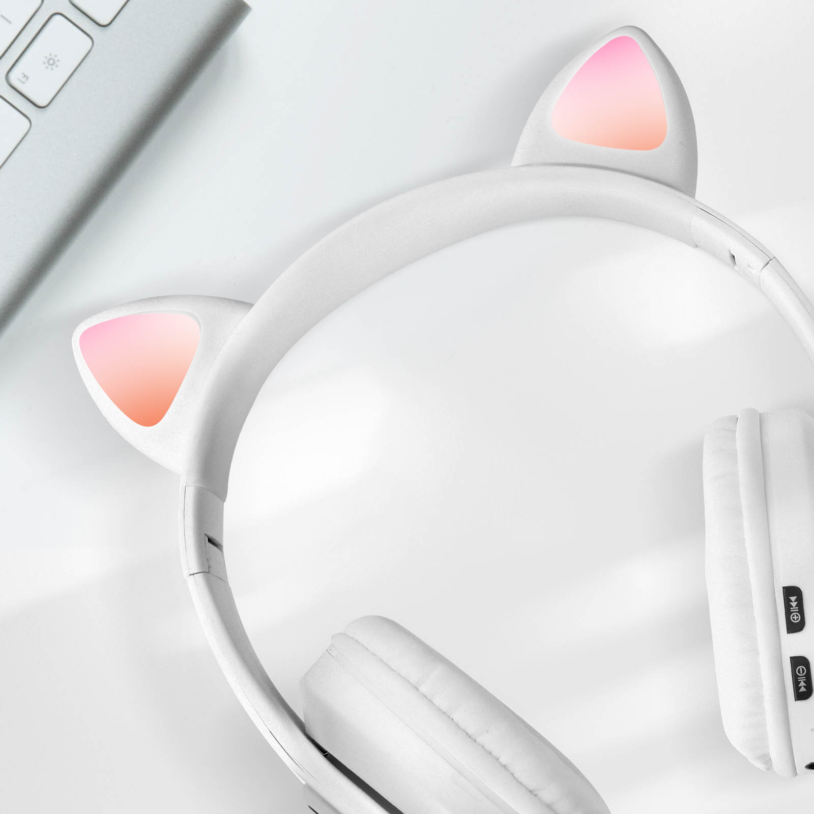 Casque blanc oreilles de chat sur surface blanche, clavier en arrière-plan.