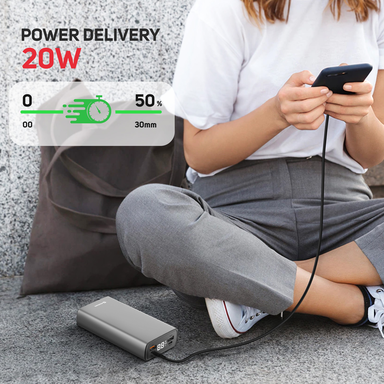 Eine Person sitzt und lädt ein Telefon von einer Powerbank auf, mit 20W und 50% Ladung in 30 Minuten.