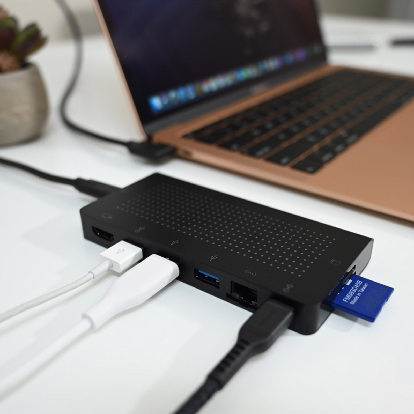 Un hub nero con diversi cavi collegati. Un laptop sullo sfondo. Scheda SD blu inserita.