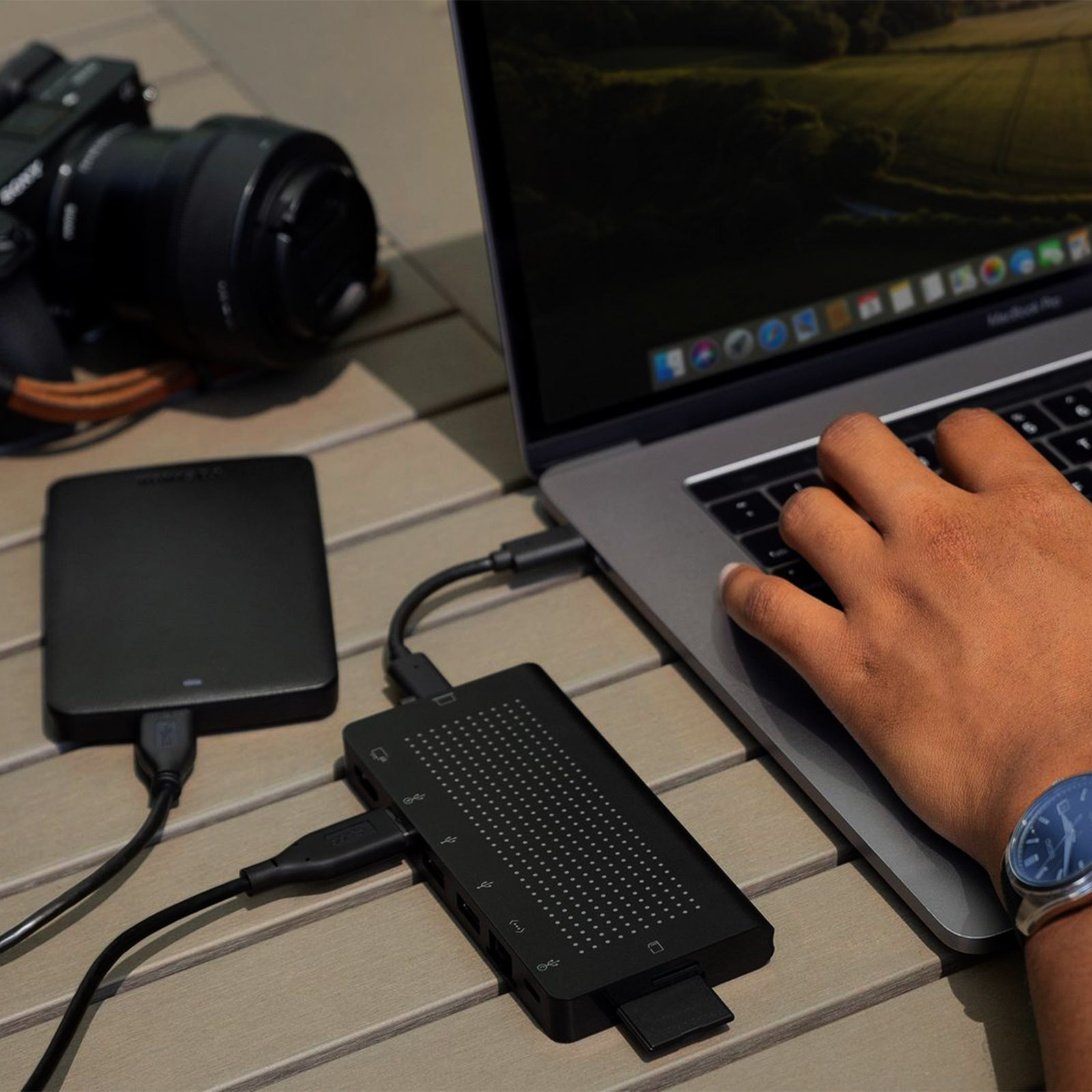 Un laptop con un hub USB collegato. Una fotocamera e un disco rigido esterno sono nelle vicinanze.