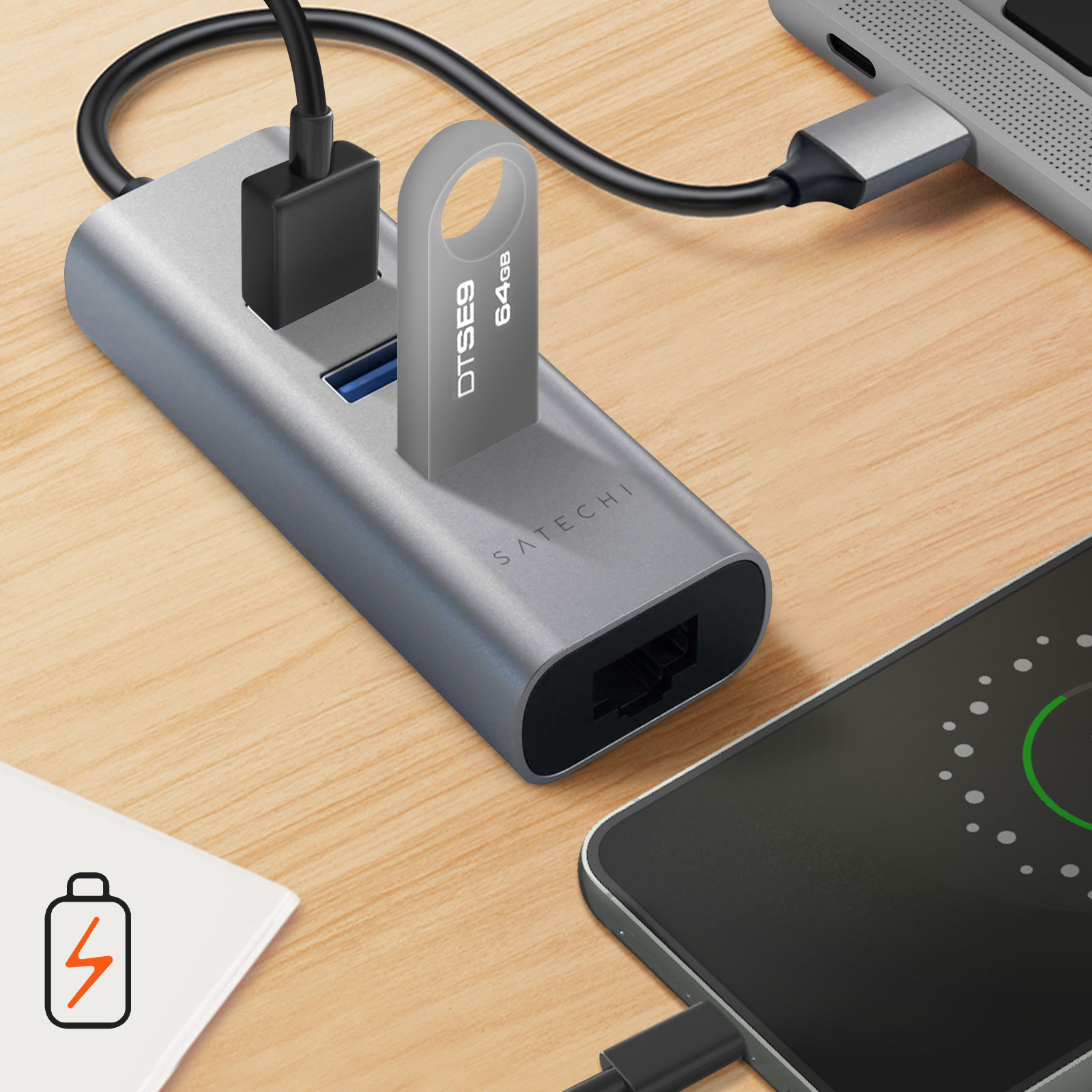 Ein silberner Hub mit angeschlossenen USB-Geräten und einem Flash-Laufwerk. Telefon und Laptop auf einem Holztisch.