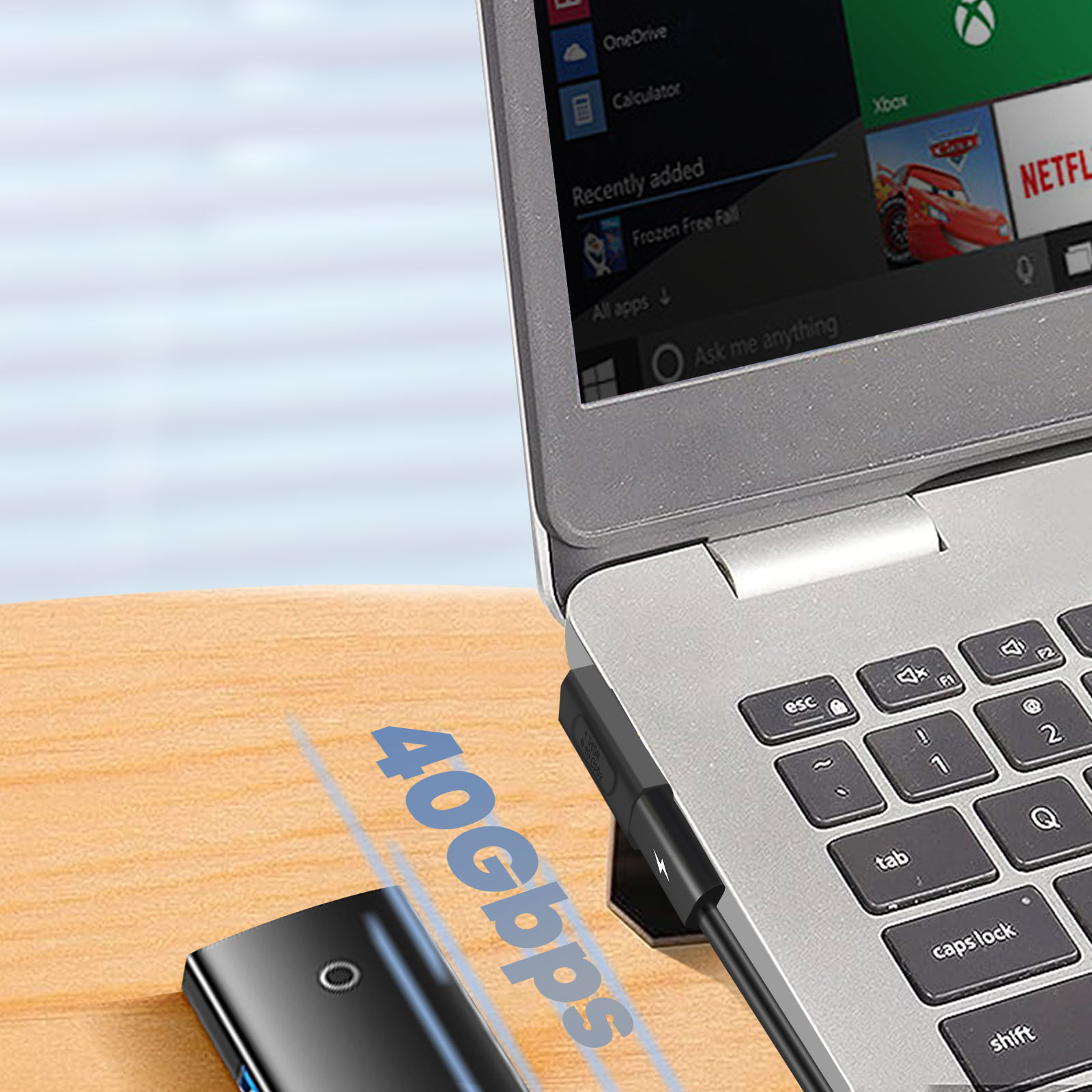 Laptop collegato a un cavo adattatore USB-C nero con l'etichetta '40 Gbps' su una superficie di legno.