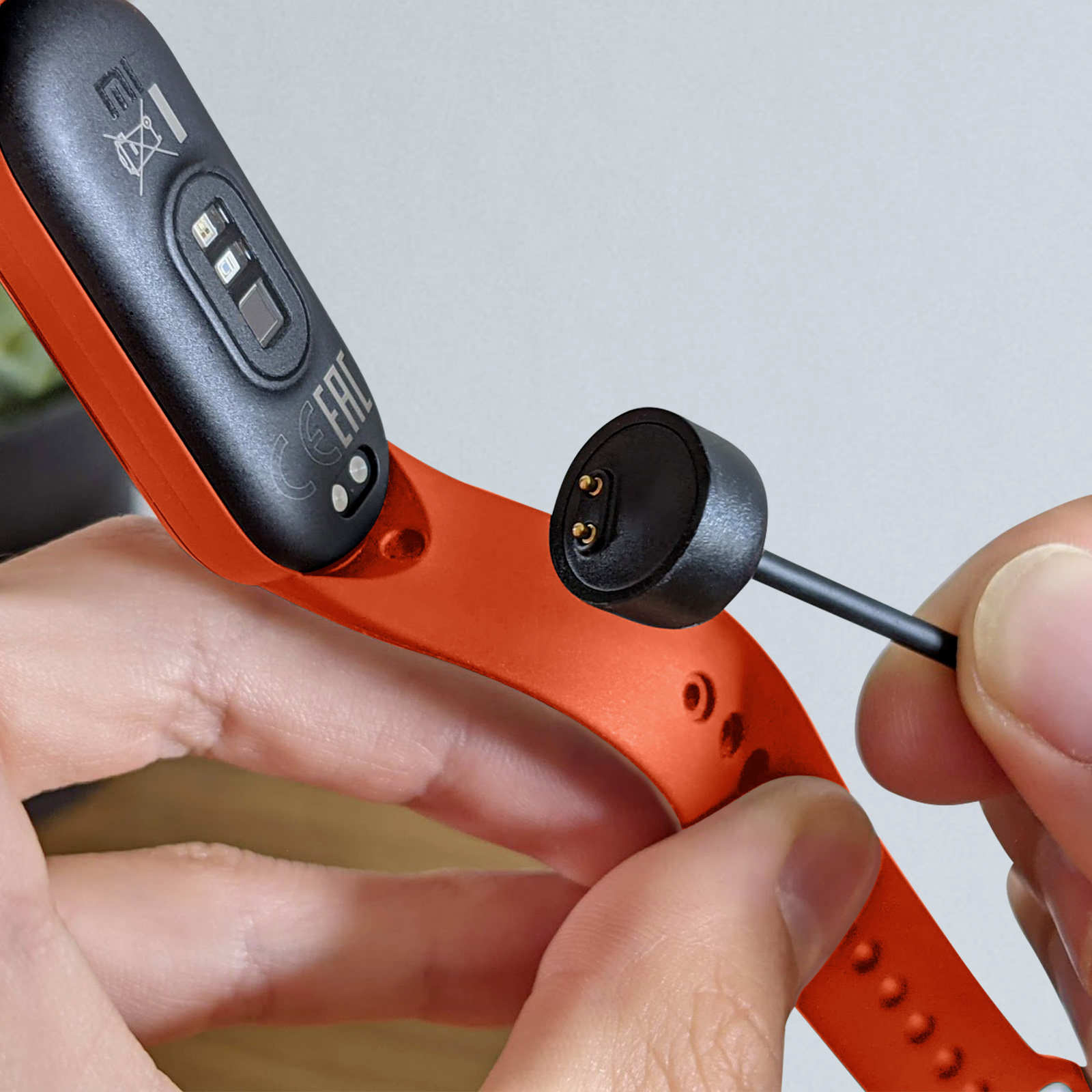 Mano che tiene uno smartwatch con cinturino arancione e caricatore collegato.