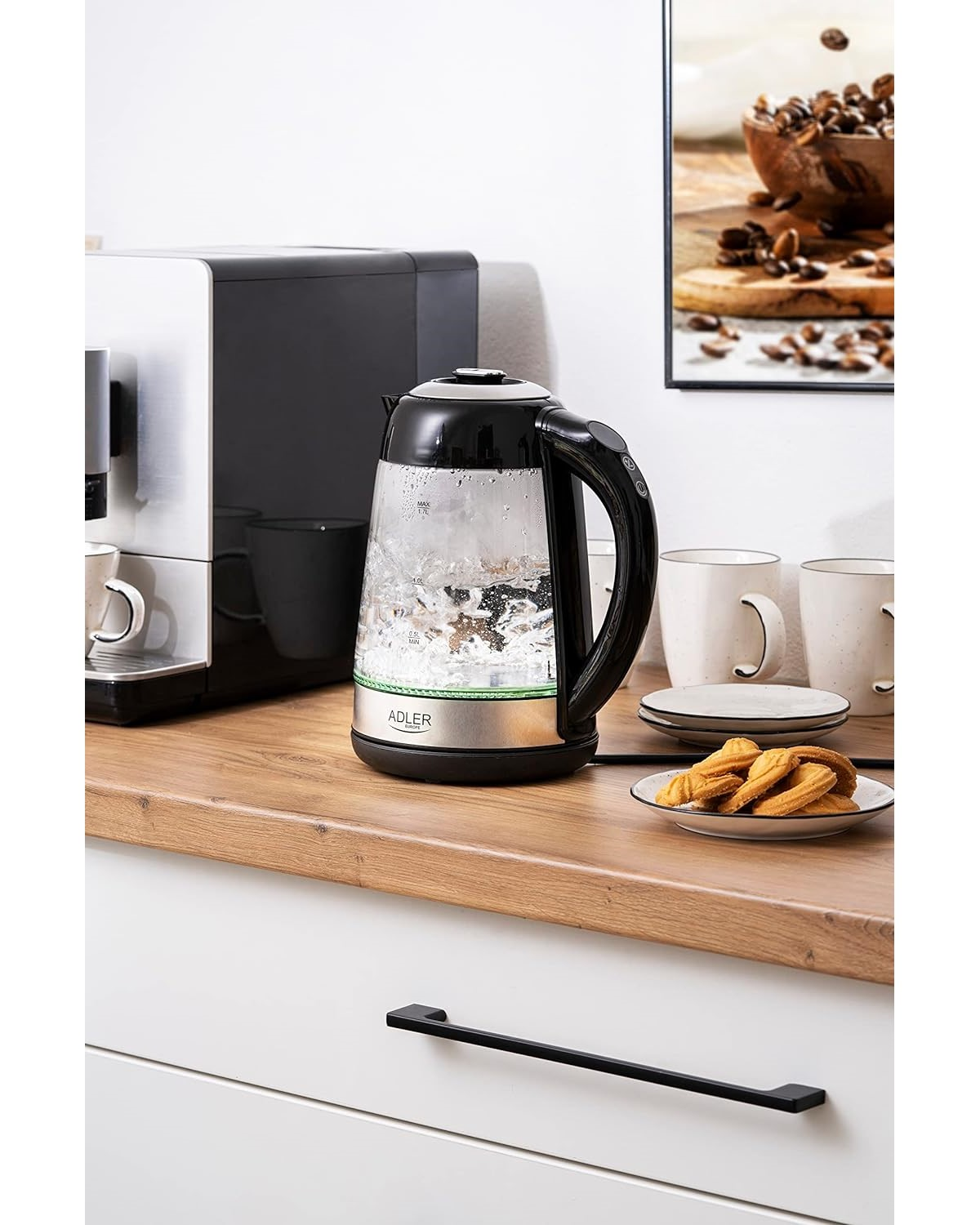 Schwarzer und silberner Wasserkocher mit kochendem Wasser. Kekse, Tassen und Kaffeemaschine vorhanden.