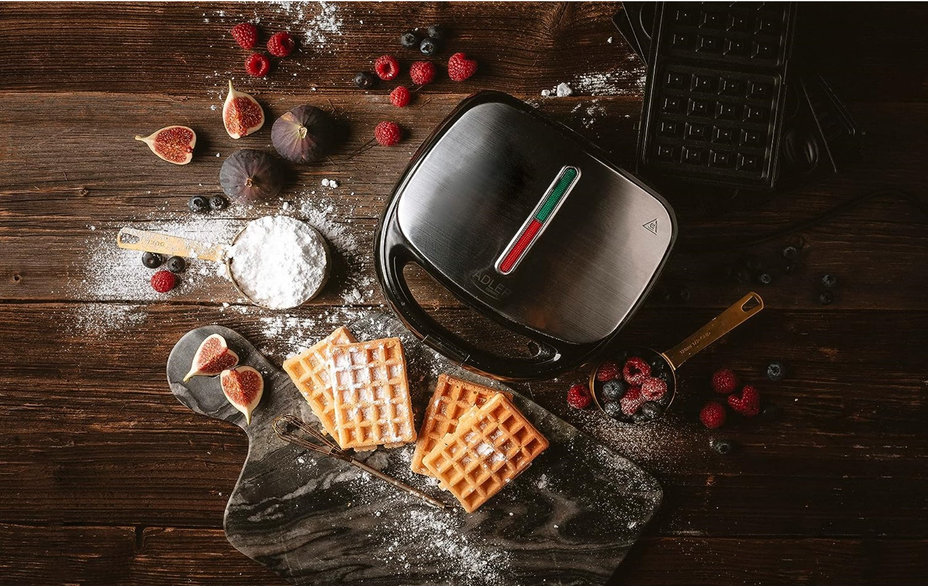 Waffeleisen mit Waffeln, Feigen, Beeren und Puderzucker auf einem Holztisch. Draufsicht.