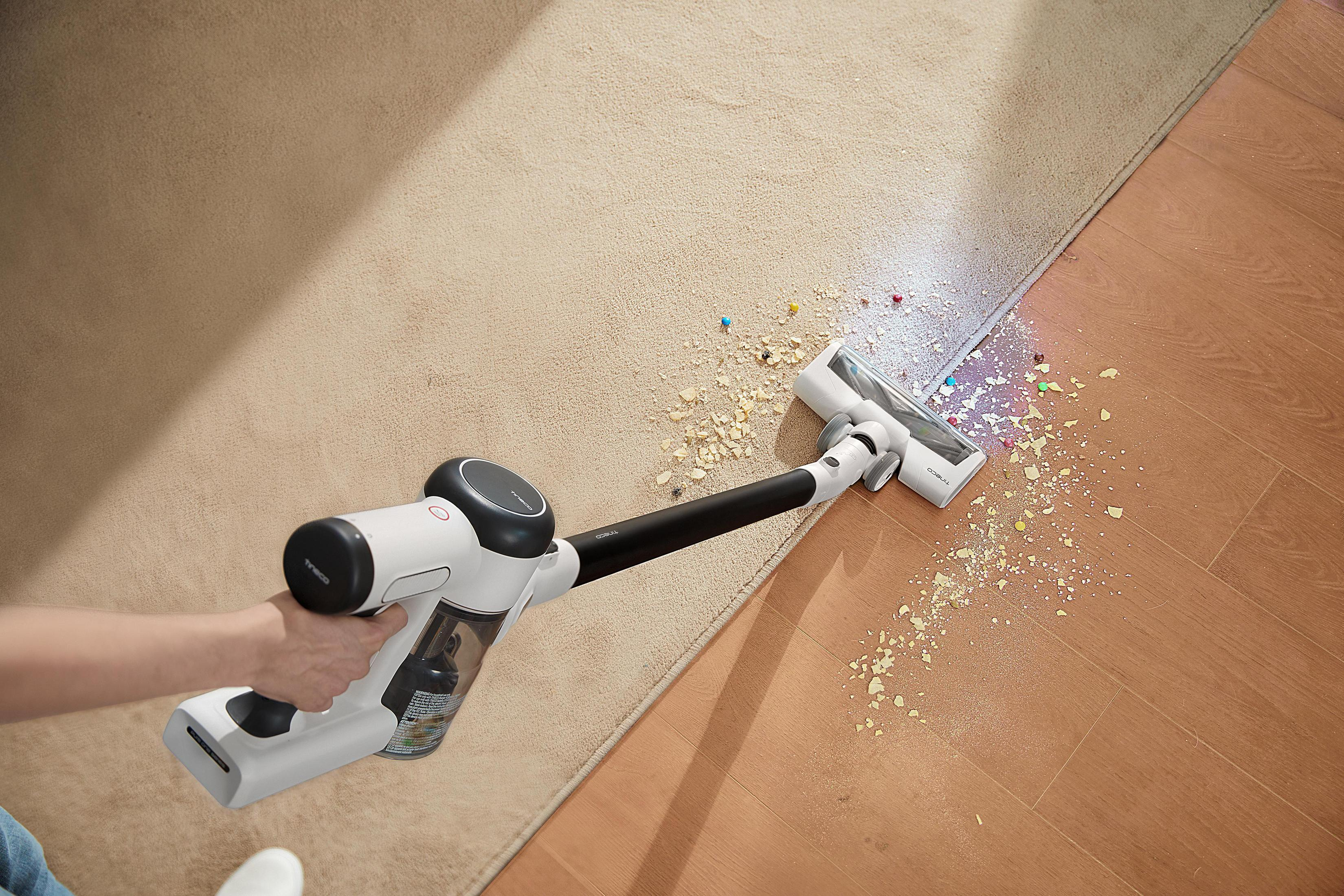 Hand holding a white and black vacuum cleaner. Vacuuming a beige carpet.