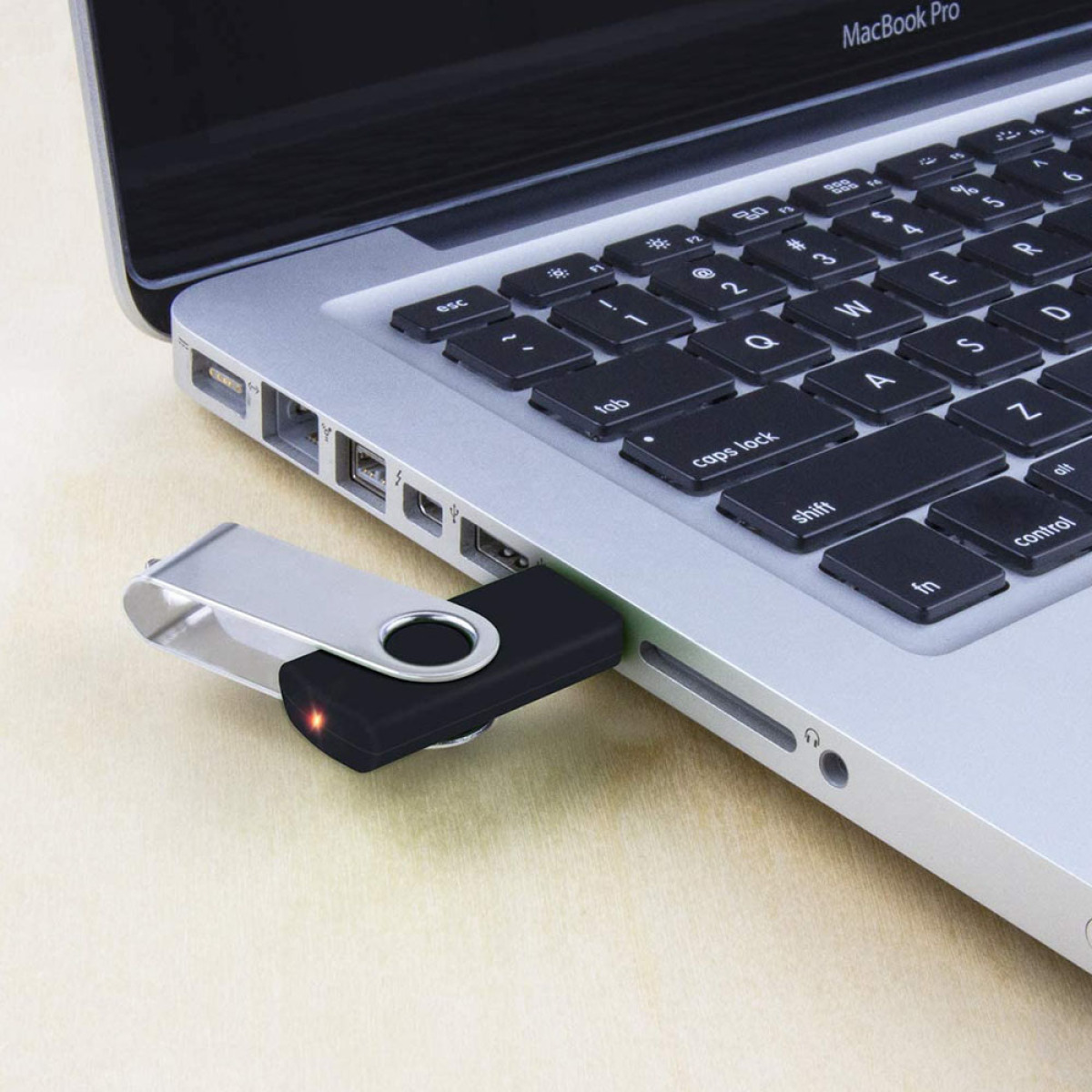 Schwarzer USB-Stick in einem silbernen Laptop. Ein rotes Licht leuchtet.