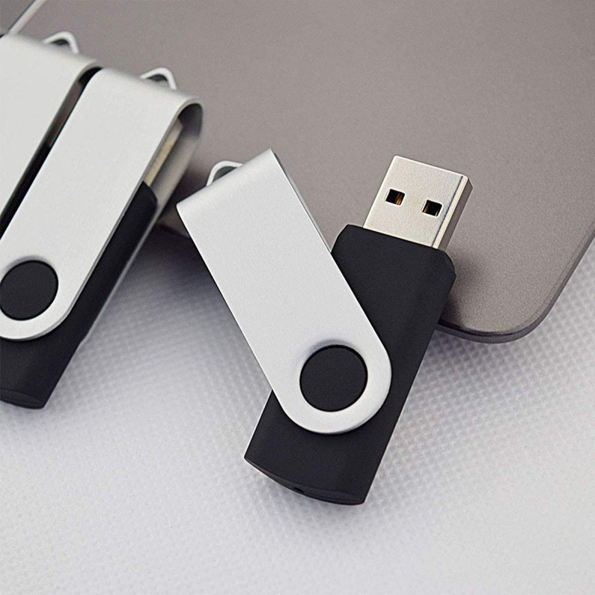 Zwei USB-Sticks, silber und schwarz, liegen auf einer hellgrauen Oberfläche. Nahaufnahme.