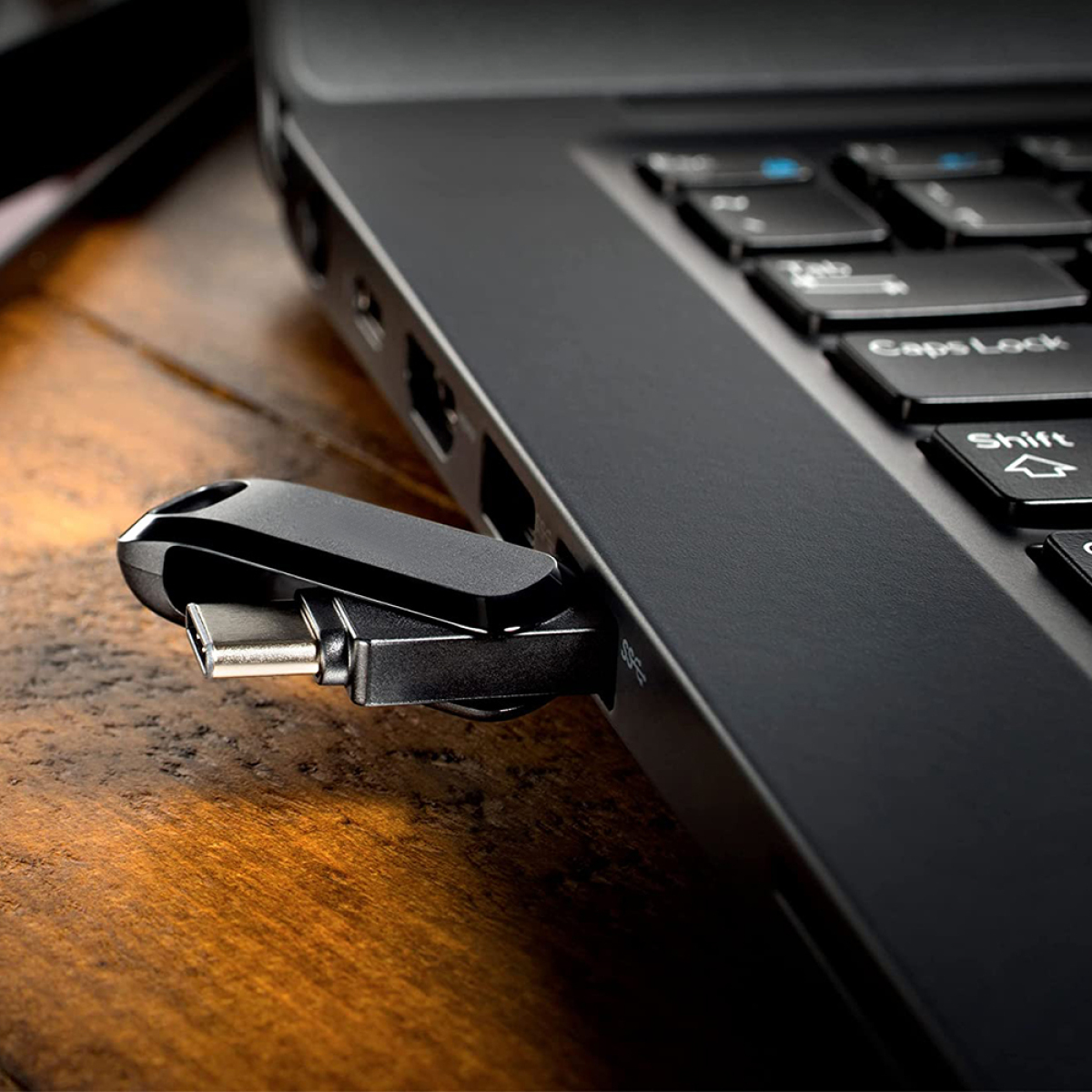 Ein schwarzer USB-C-Adapter steckt in einem schwarzen Laptop, auf Holz.