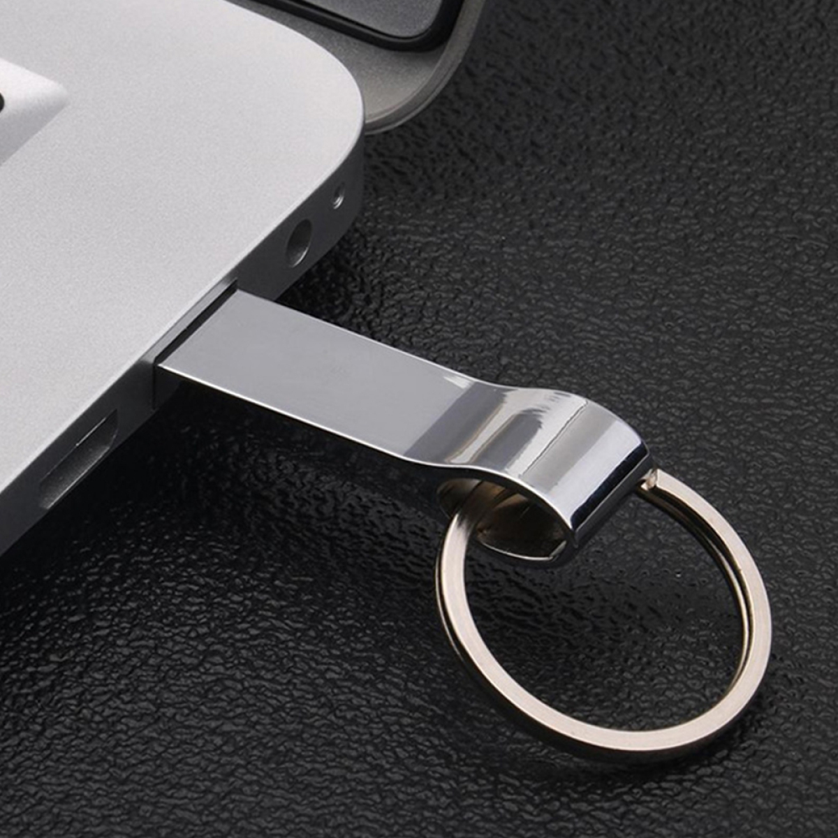 Silberner USB-Stick in einen Laptop gesteckt, Schlüsselring angebracht, auf schwarzer Oberfläche.