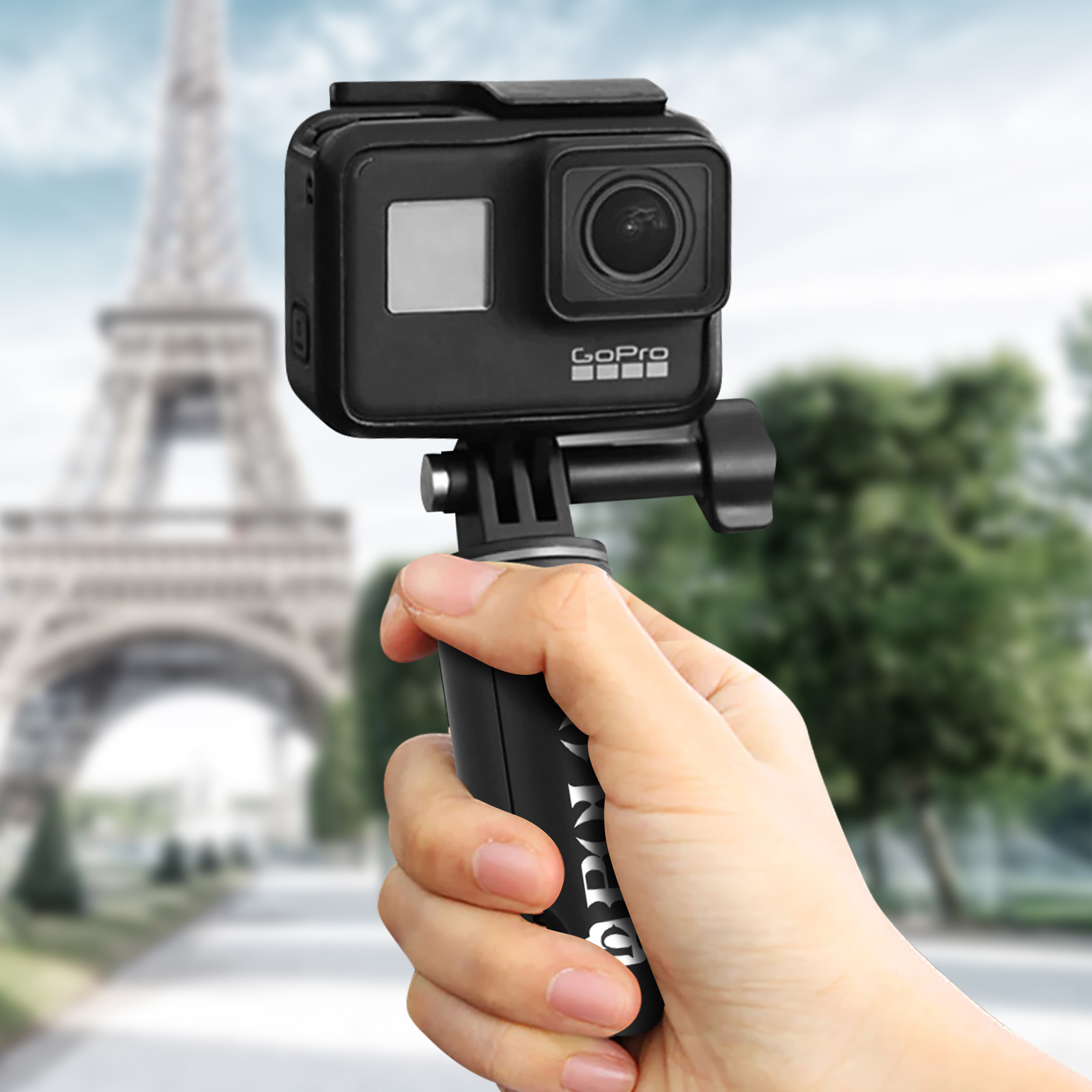 Mano che tiene una fotocamera GoPro nera. La Torre Eiffel è sfocata sullo sfondo.