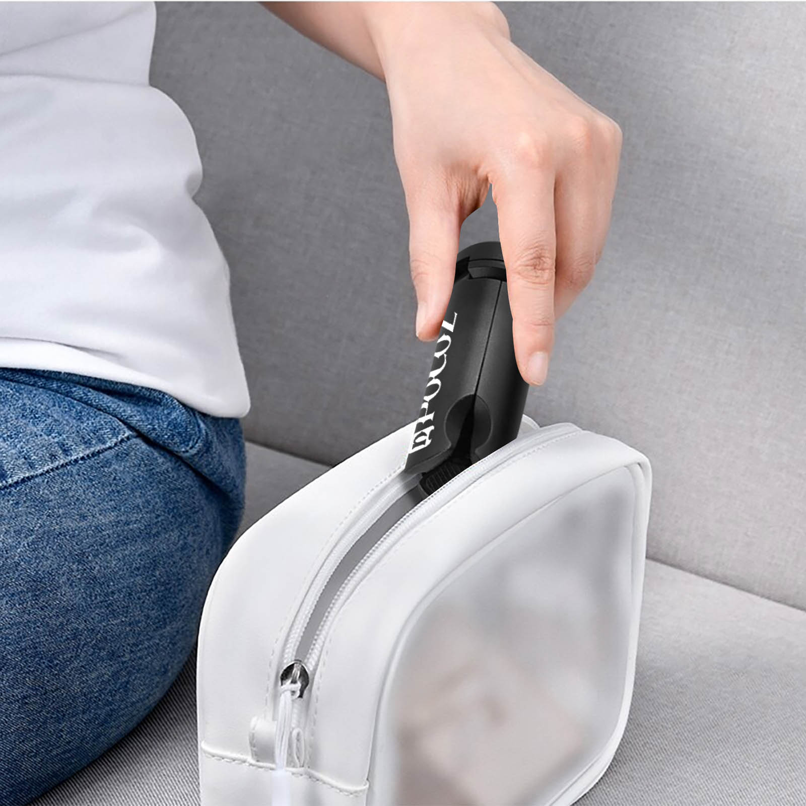 Una mano inserisce una spazzola nera in una borsa trasparente bianca. Lo sfondo è un divano bianco.