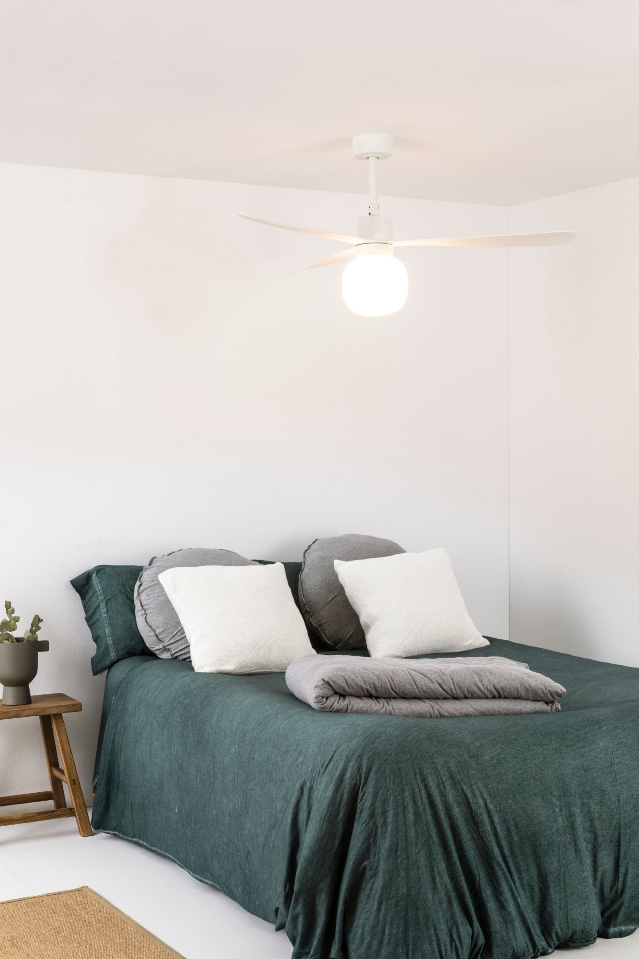 Schlafzimmer mit Bett, weißem Deckenventilator, weißen Wänden und kleinem Holzschemel.