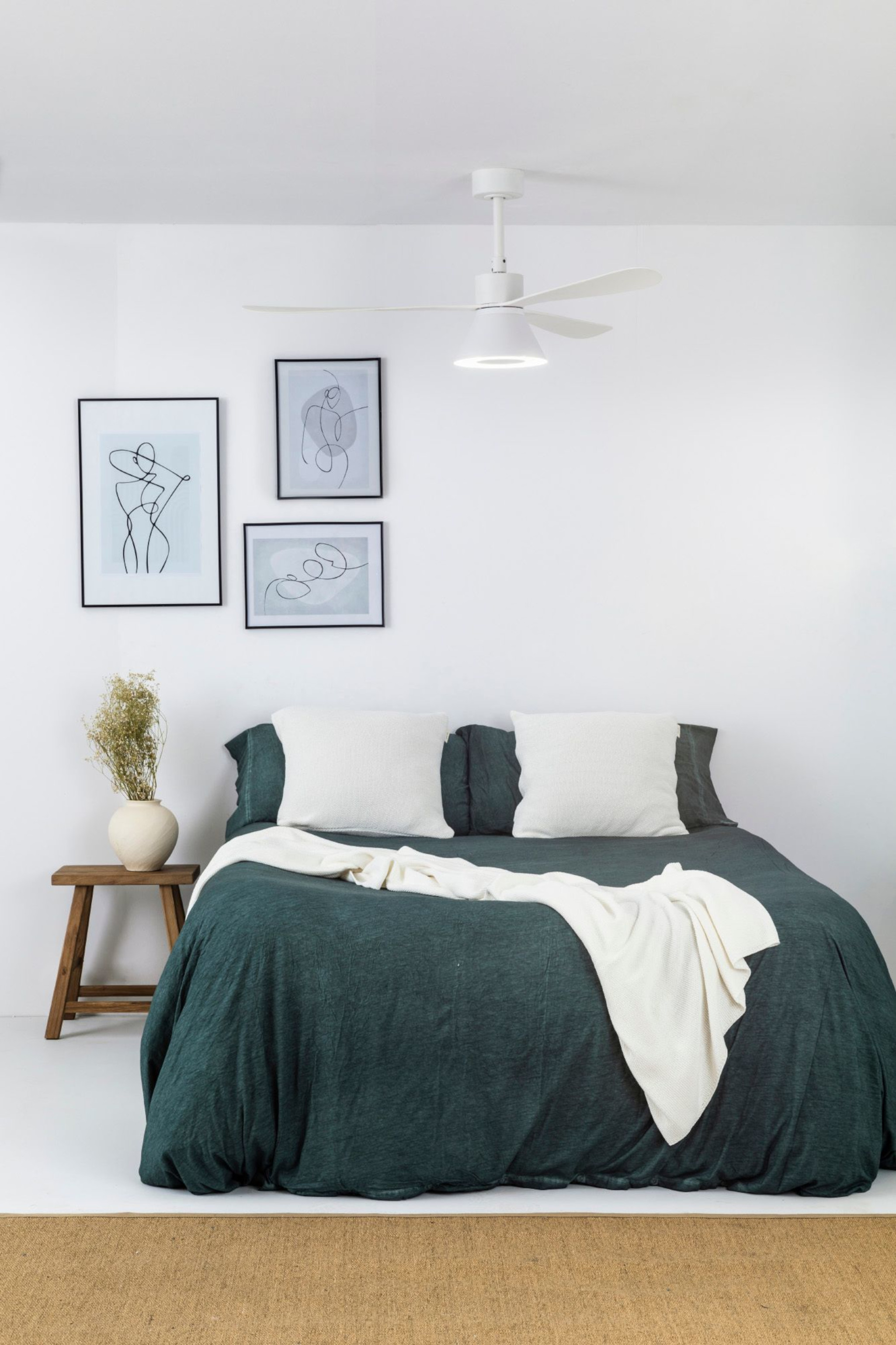 Ein Schlafzimmer mit Bett, Kunst und Deckenventilator. Das Bett hat eine grüne Bettdecke.