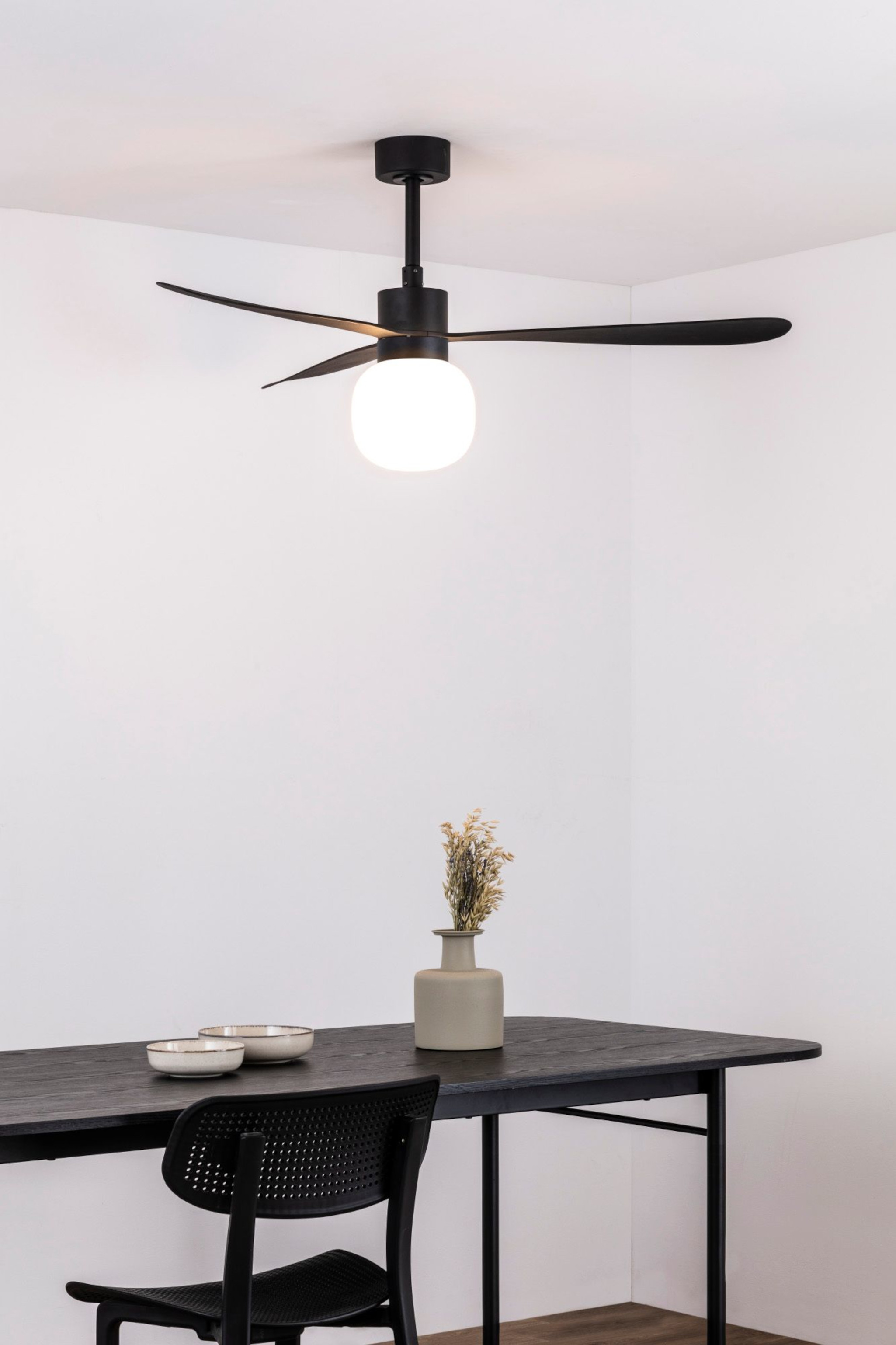 Ein schwarzer Deckenventilator mit drei Flügeln und einem weißen Licht, über einem Tisch mit Dekoration.