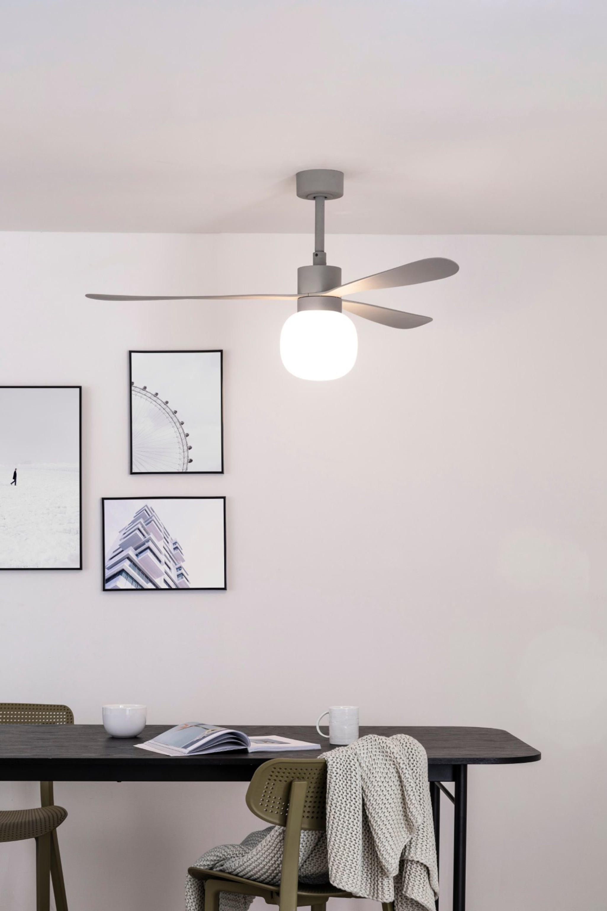 Deckenventilator mit Glühbirne, gerahmte Bilder, Tisch und Stühle.