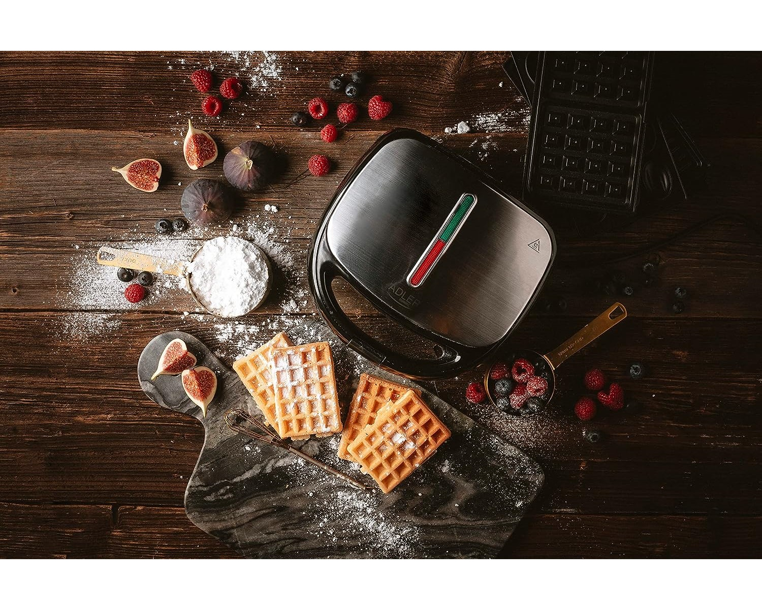 Waffeln und Zutaten auf einem Holztisch. Beeren, Feigen und Puderzucker sind drumherum angeordnet.