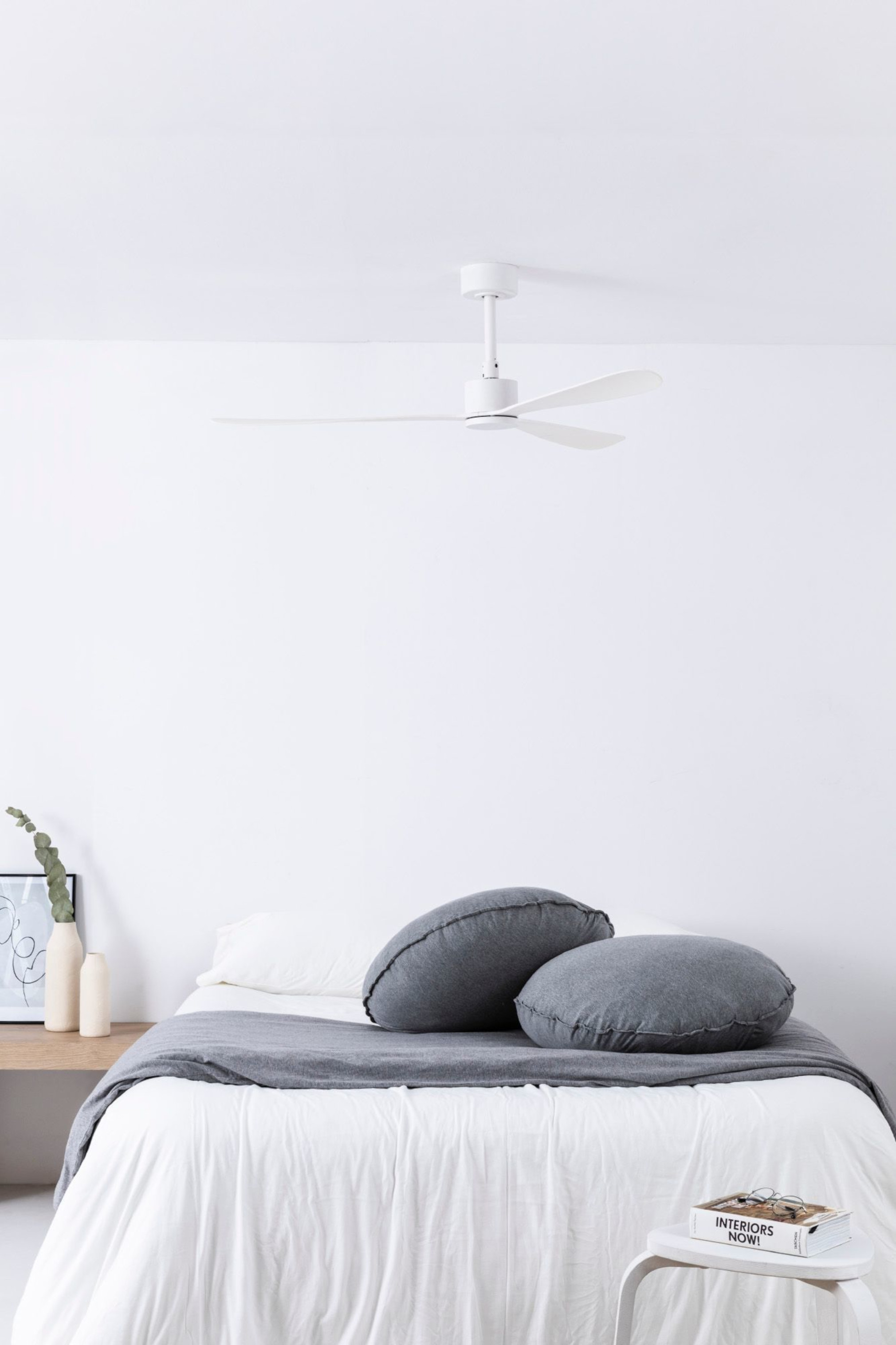 Ein Schlafzimmer mit einem weißen Deckenventilator und zwei grauen Kissen auf einem Bett mit weißem Laken.