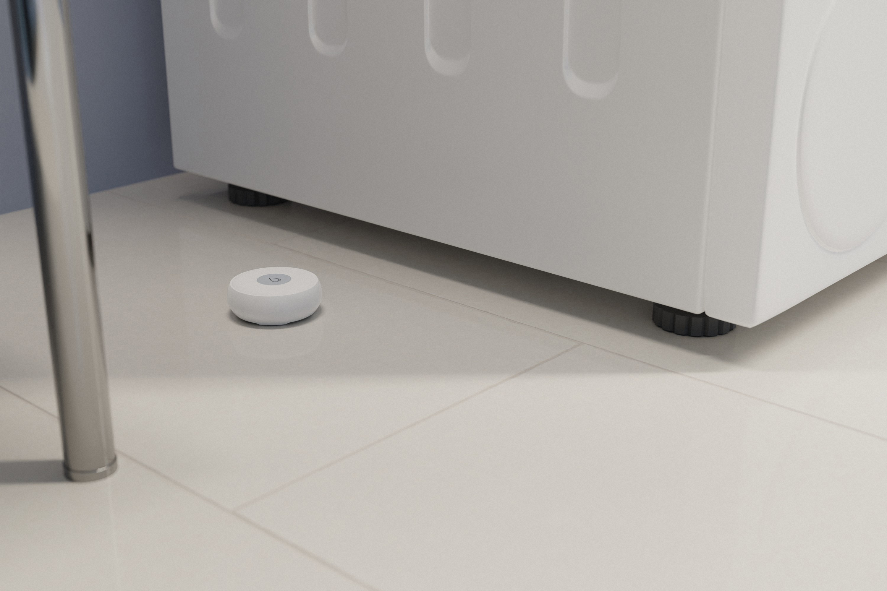 Ein weißer Smart-Home-Sensor auf einem weißen Fliesenboden neben einer Waschmaschine.