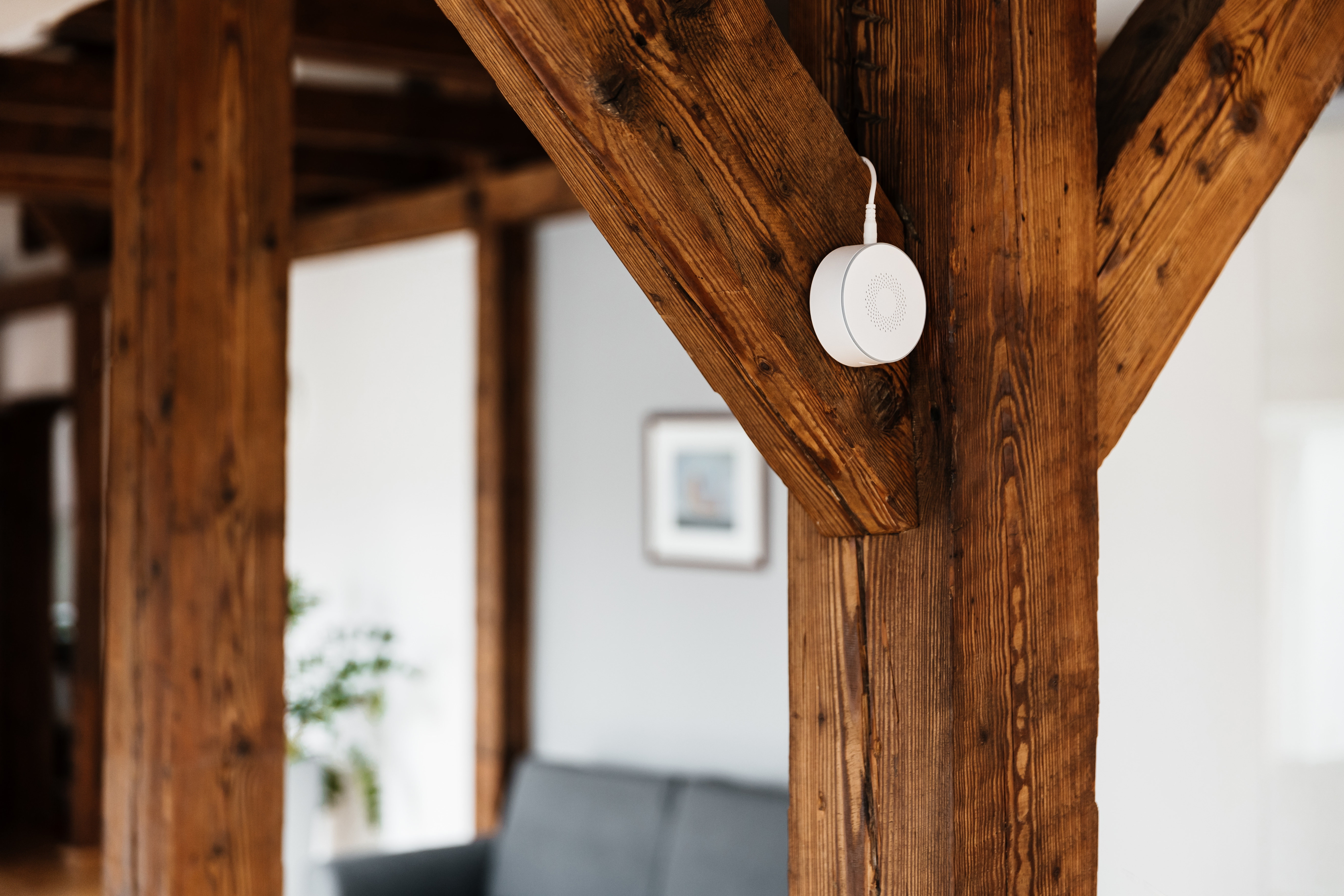 Ein weißer Lautsprecher ist an einem Holzbalken in einem Haus montiert. Die Holzbalken sind braun.