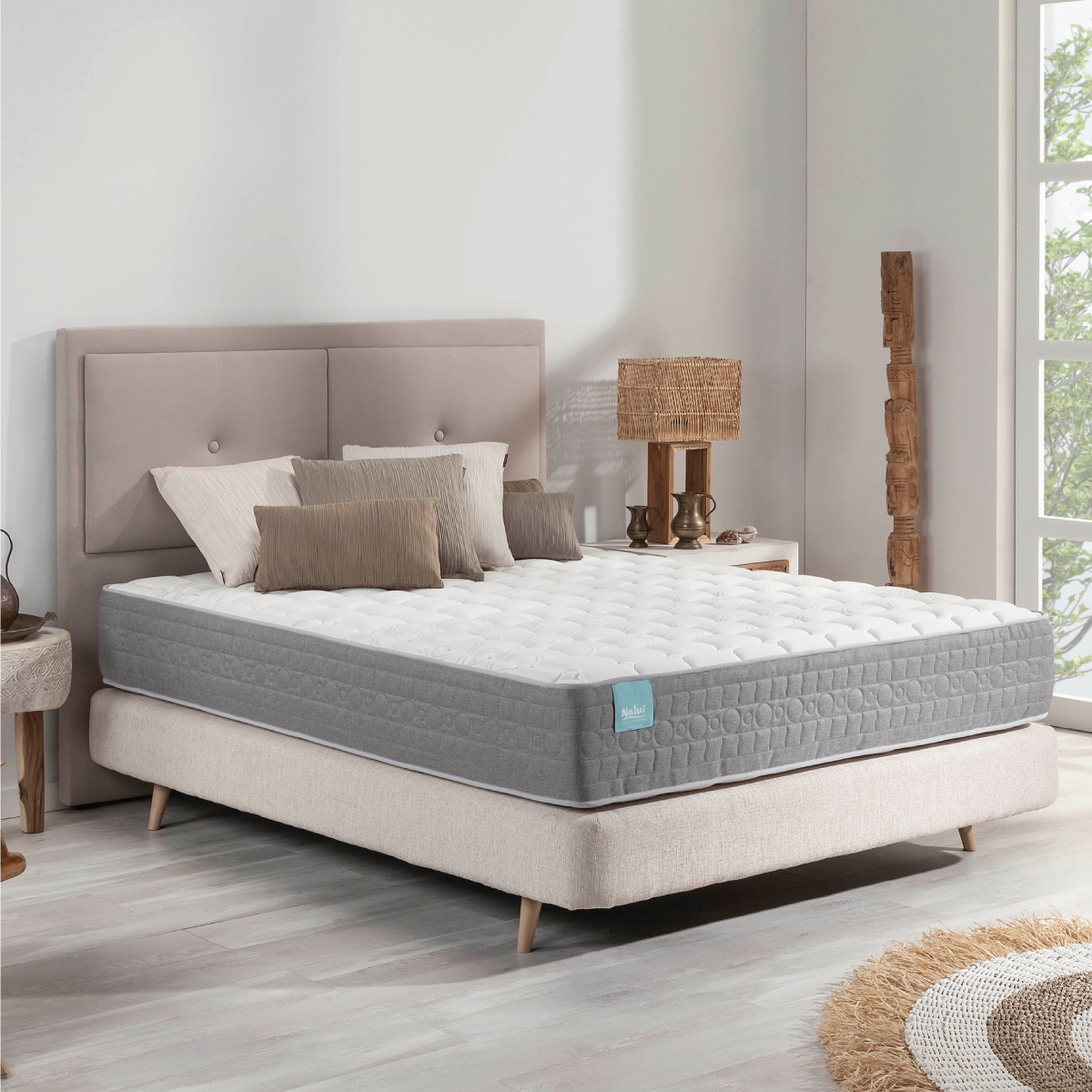 Escena de dormitorio con cama, almohadas y cabecero. Hay una ventana y una mesita de noche.