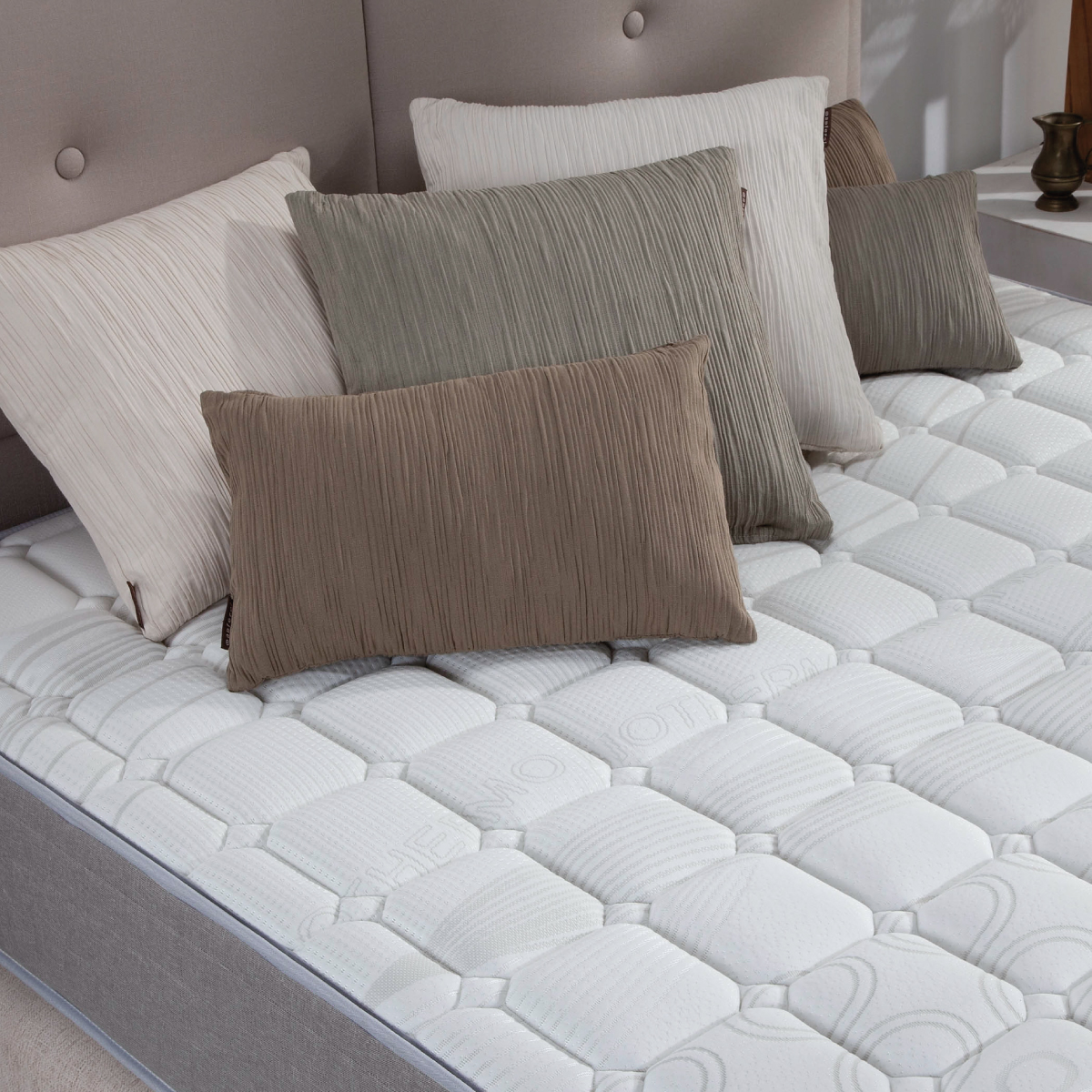 Cama con almohadas de varios colores y formas. El colchón es blanco.