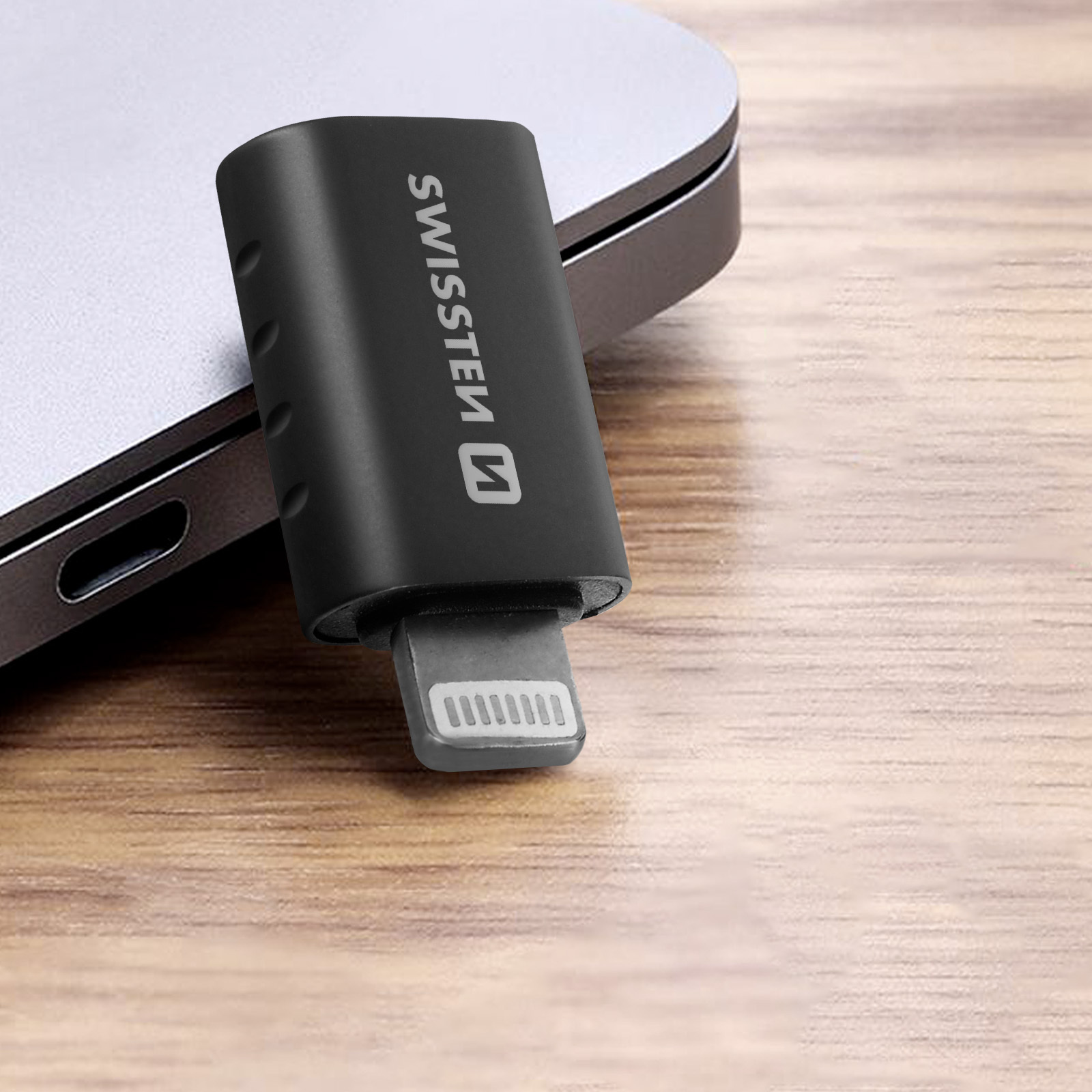 Un adaptateur noir avec un connecteur USB. L'adaptateur est devant un ordinateur portable argenté.