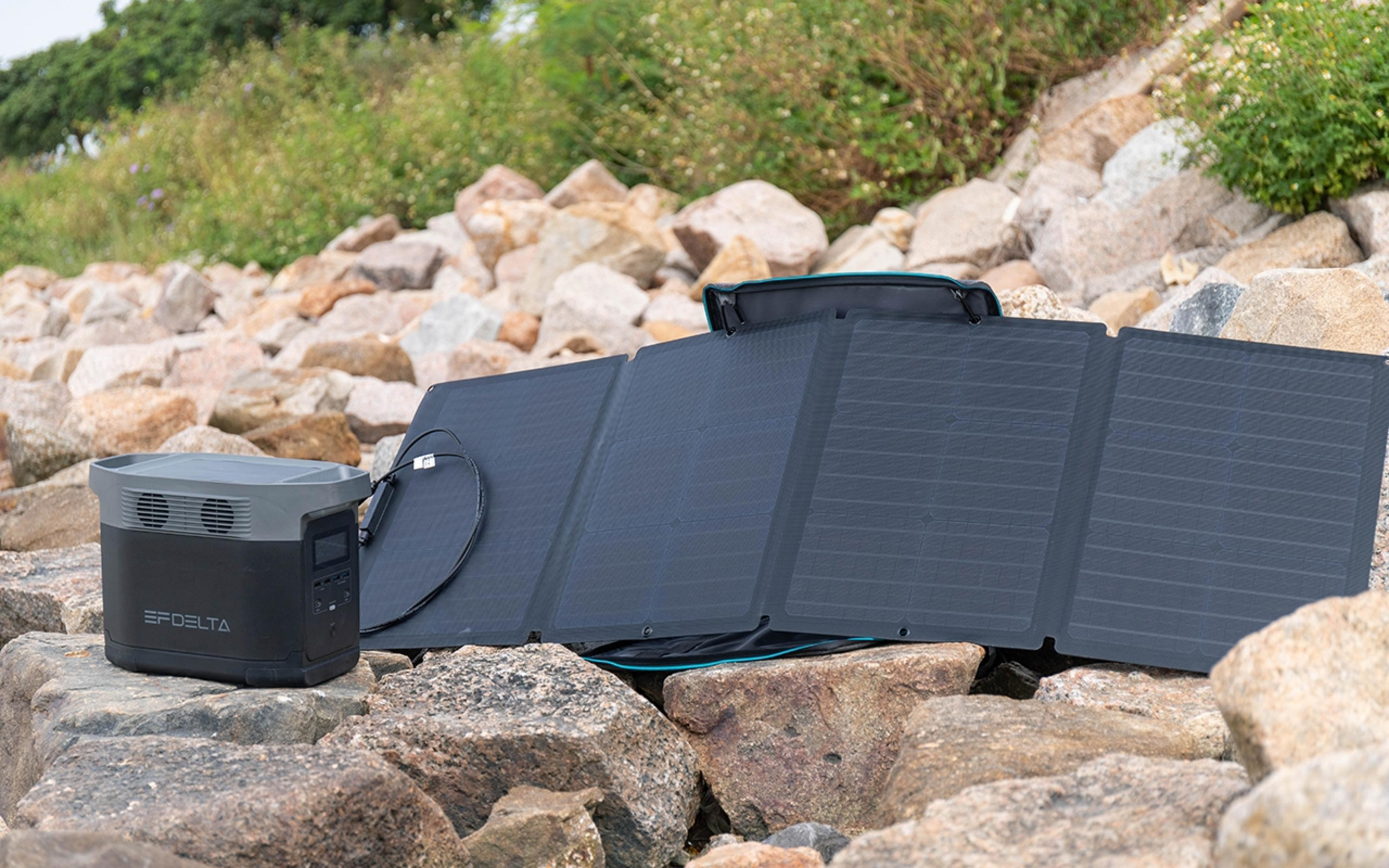 Instalacja paneli słonecznych na skałach. Czarna elektrownia po lewej, a złożony panel słoneczny po prawej. Zielona trawa z tyłu.