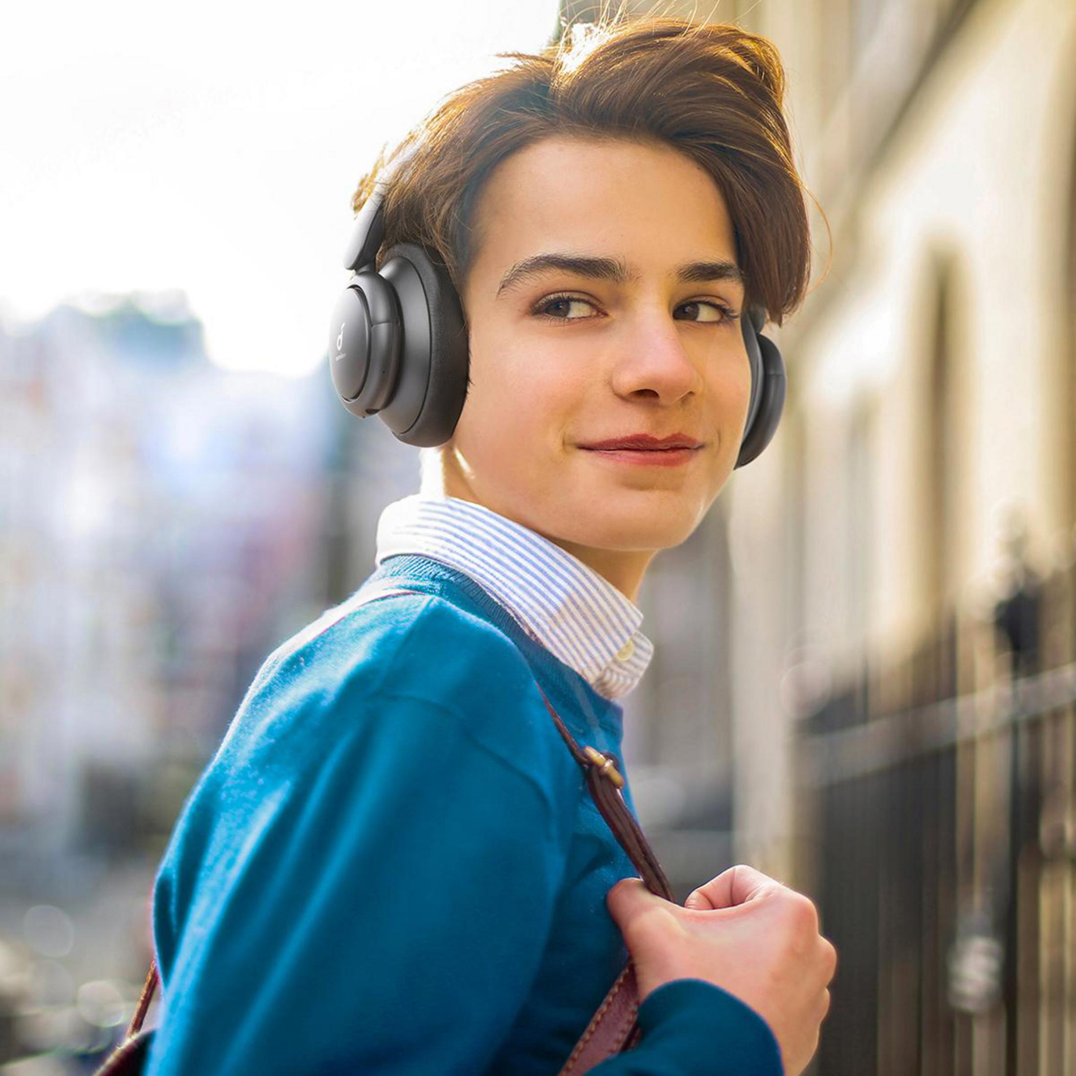 Un joven con auriculares negros, mirando por encima del hombro con una sonrisa.
