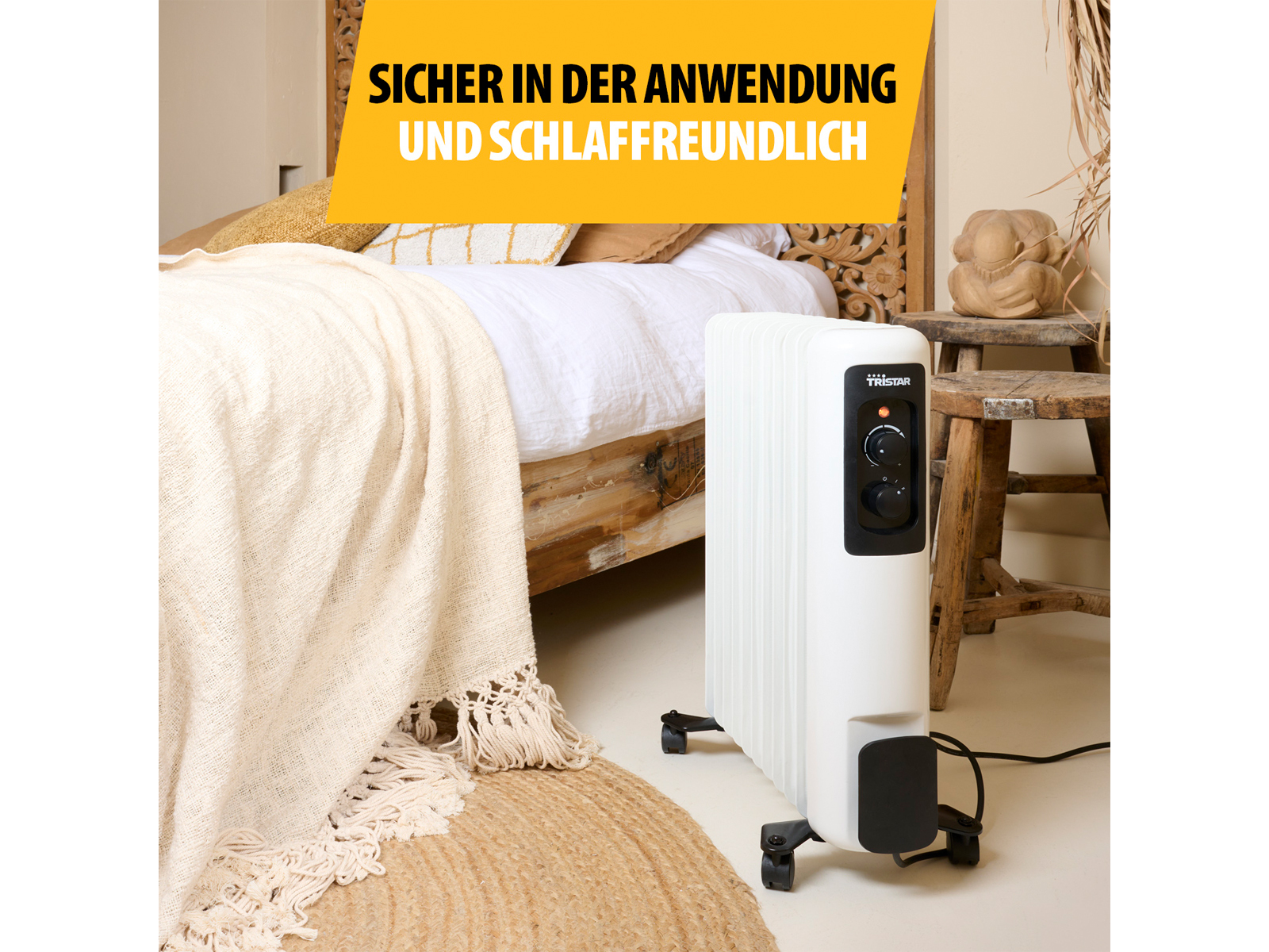 Biały grzejnik olejowy Tristar obok łóżka z kocem i dywanem.