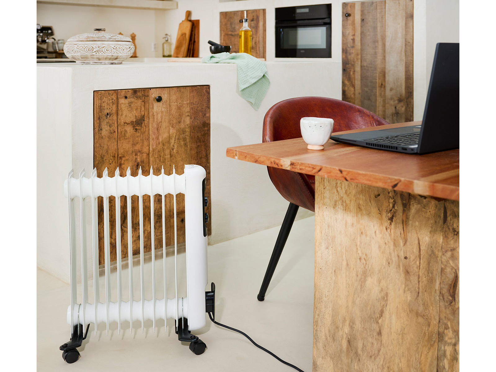 Biały grzejnik elektryczny na kółkach w otoczeniu kuchni obok drewnianego stołu.
