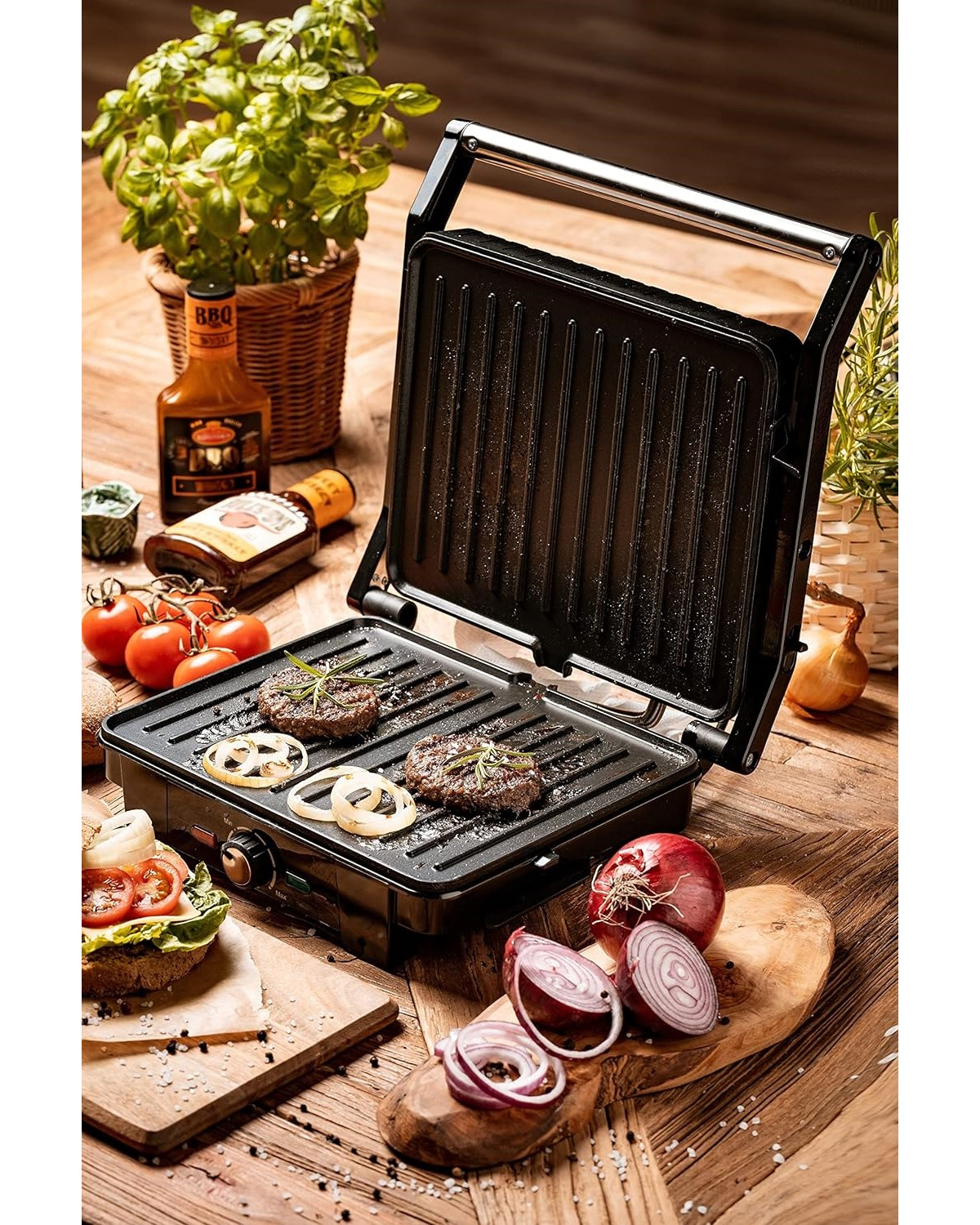Ein offener Grill mit zwei Burgern, Zwiebeln und anderen Zutaten. Er steht auf einem Holztisch.
