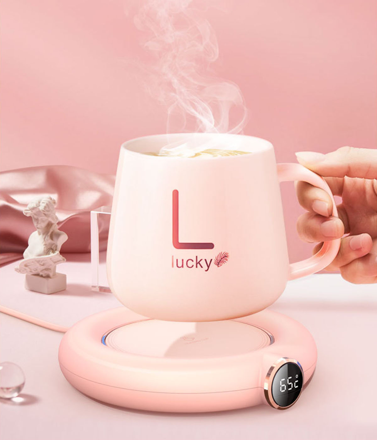 Rosa Tasse auf einem rosa Wärmer, Dampf steigt auf. Hand hält die Tasse.