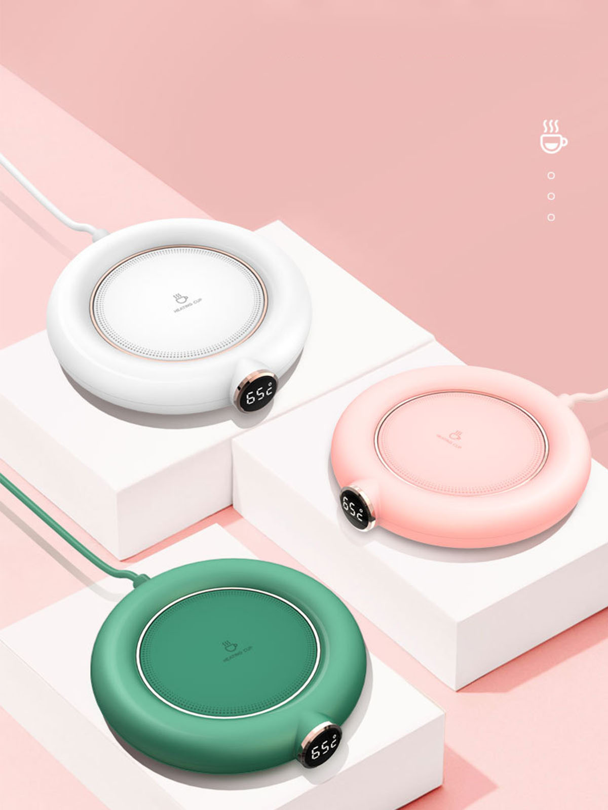 Drei runde elektrische Tassenwärmer, weiß, rosa und grün, auf weißen Podesten.