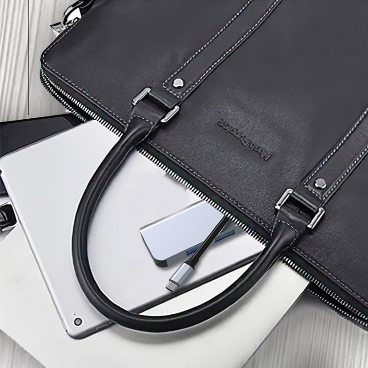 Eine schwarze Ledertasche mit einem Tablet und anderen Gegenständen darin. Ein USB-C-Hub ist ebenfalls sichtbar.