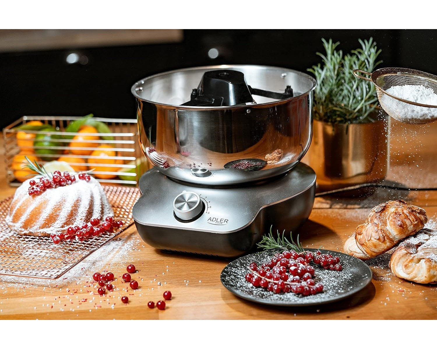 Ein silber-grauer Standmixer mit Schüssel und Zubehör, mit Backwaren drumherum.