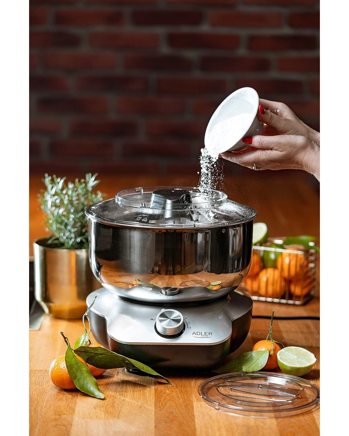 Eine Person, die Mehl in einen Mixer gibt, mit Mandarinen und Limette.