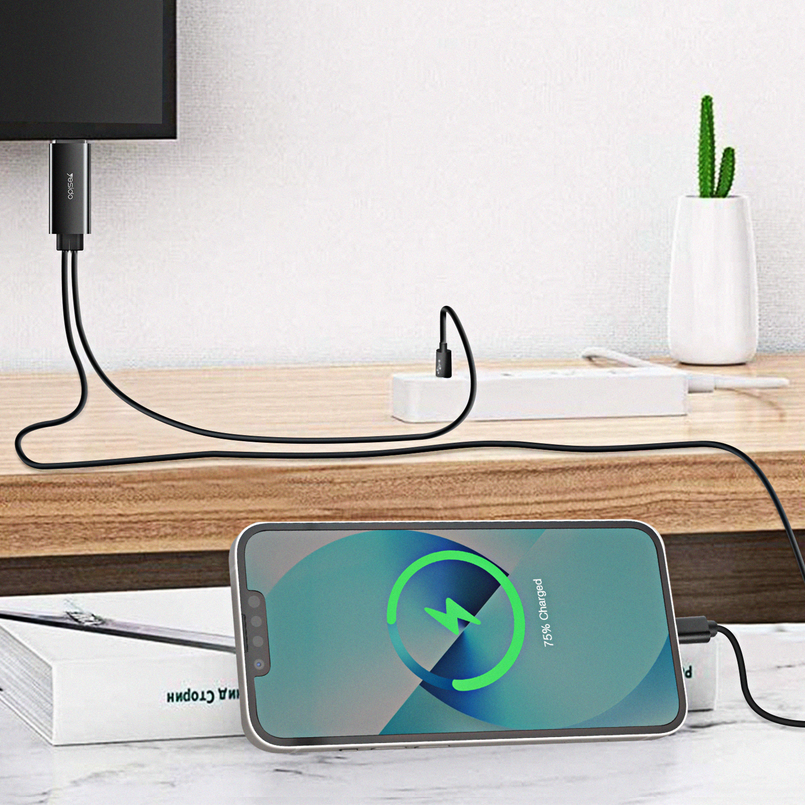 Smartphone, das auf einem Holzschreibtisch geladen wird, mit Fernseher und Pflanze im Hintergrund.