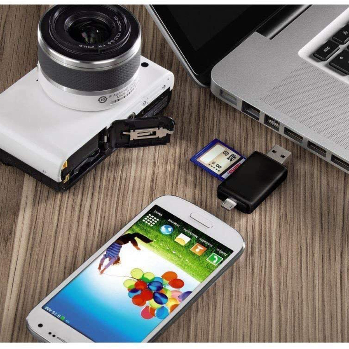Eine Kamera, ein Telefon, ein Laptop, eine SD-Karte und ein USB-Adapter liegen auf einem Holztisch.